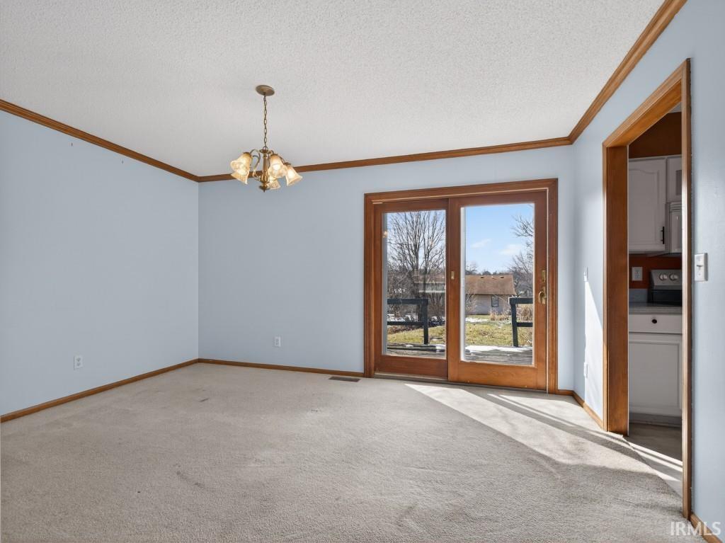 Carpeted empty room featuring crown molding, a chandelier, and a textured ceiling