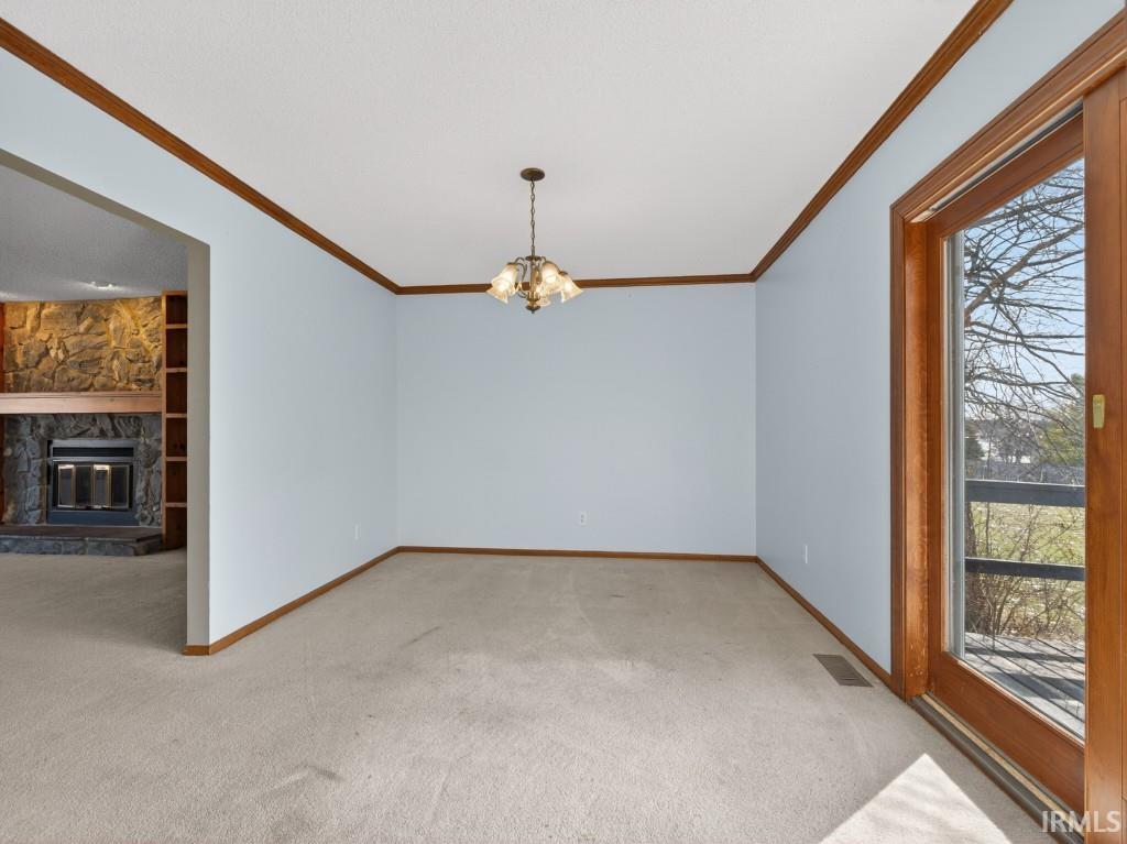 Unfurnished dining area with light colored carpet, hanging lights, a stone fireplace, built in features, and ornamental molding