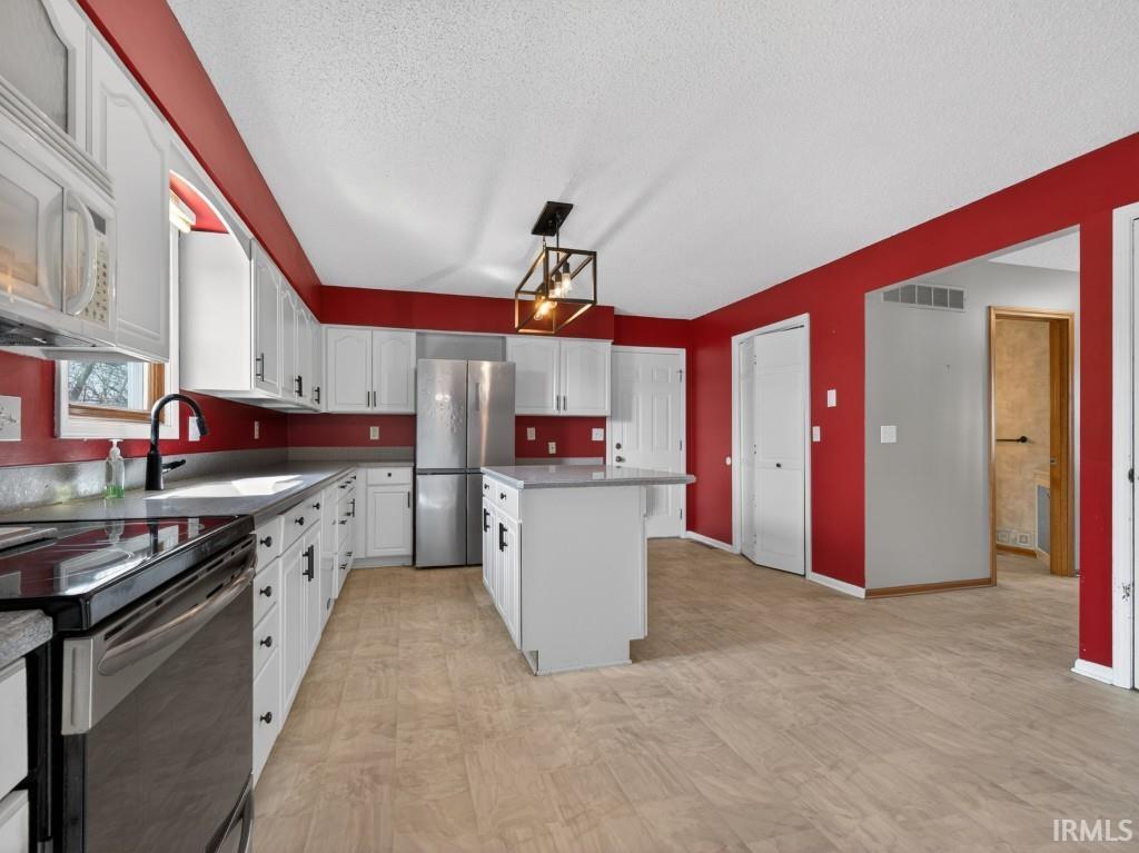 Kitchen featuring freestanding refrigerator, electric range, white cabinets, a center island, and white microwave
