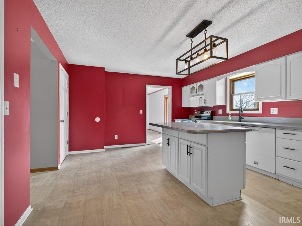 Kitchen featuring white cabinetry, white appliances, a kitchen island, a textured ceiling, and light wood-style floors