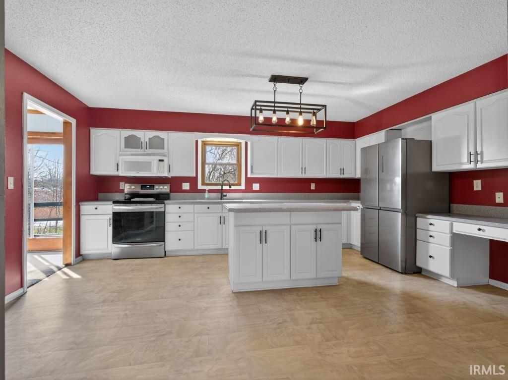 Kitchen with stainless steel appliances, hanging light fixtures, white cabinetry, a textured ceiling, and a center island