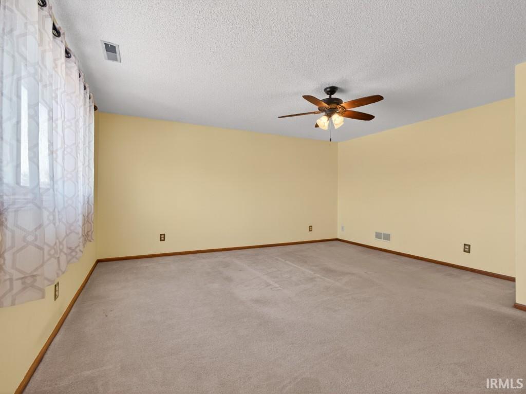 Unfurnished room featuring light colored carpet, a textured ceiling, and a ceiling fan
