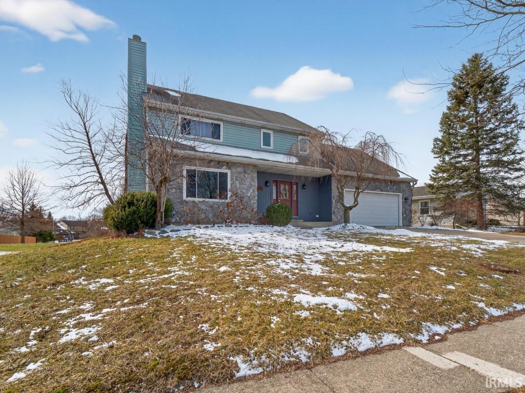 Traditional-style house featuring stone siding, an attached garage, a chimney, and a porch