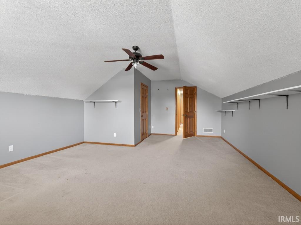 Additional living space with light carpet, a textured ceiling, and ceiling fan