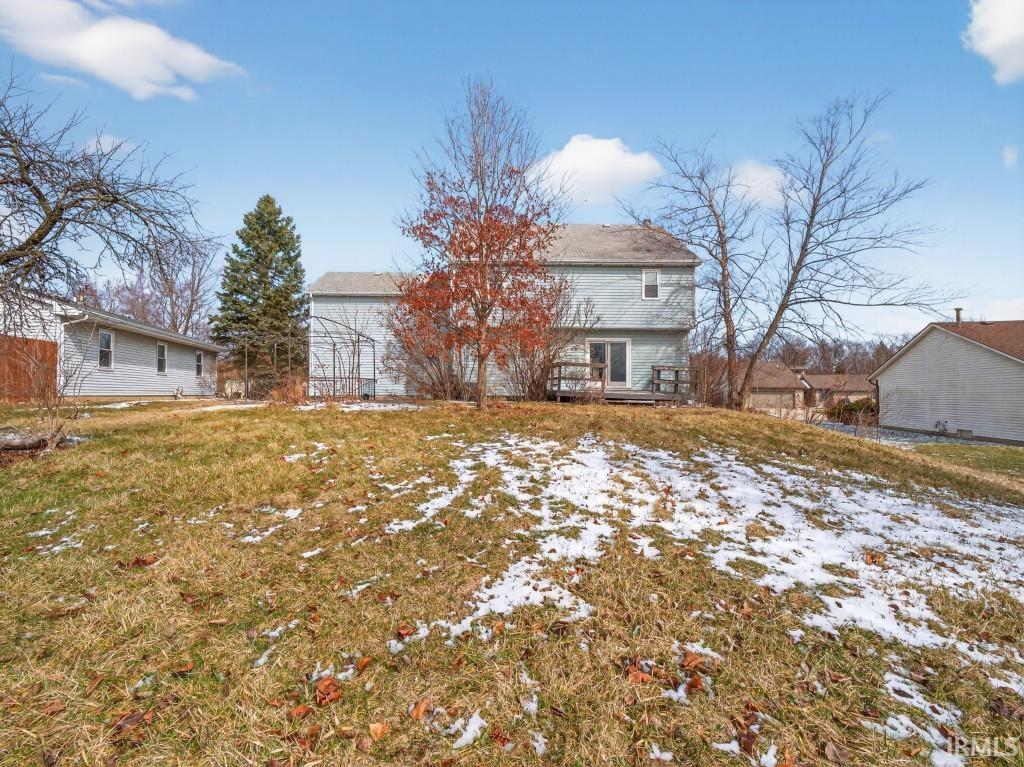 Snow covered back of property with a wooden deck and a yard