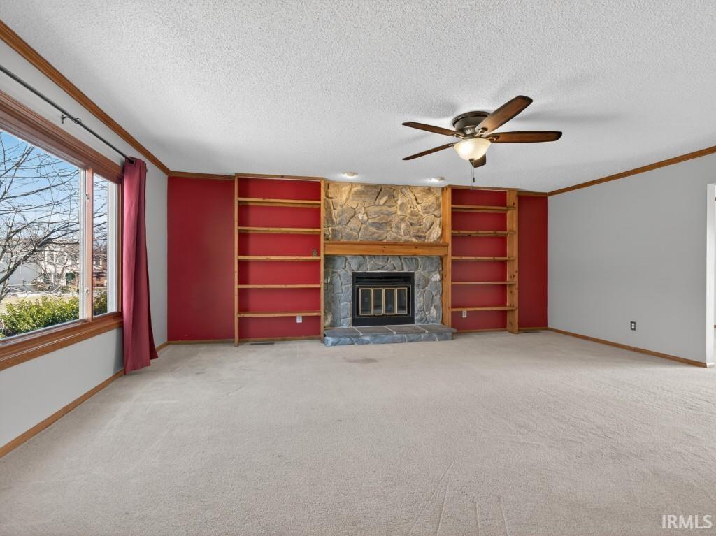 Unfurnished living room with built in features, light carpet, crown molding, a fireplace, and ceiling fan