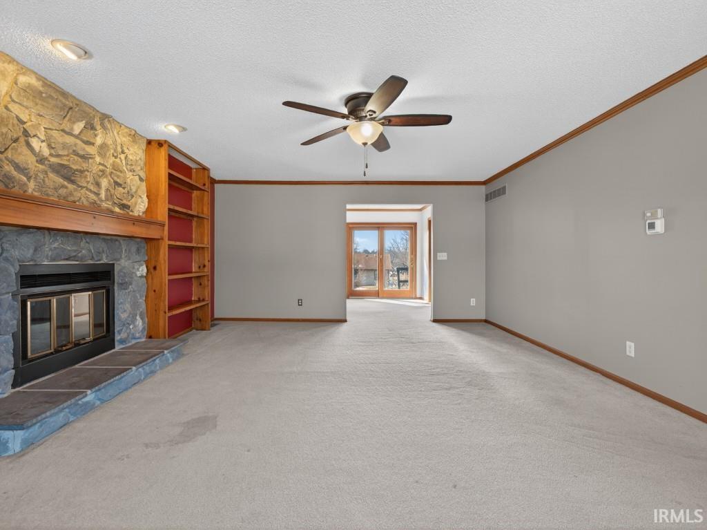 Unfurnished living room featuring light colored carpet, a fireplace, a ceiling fan, ornamental molding, and a textured ceiling