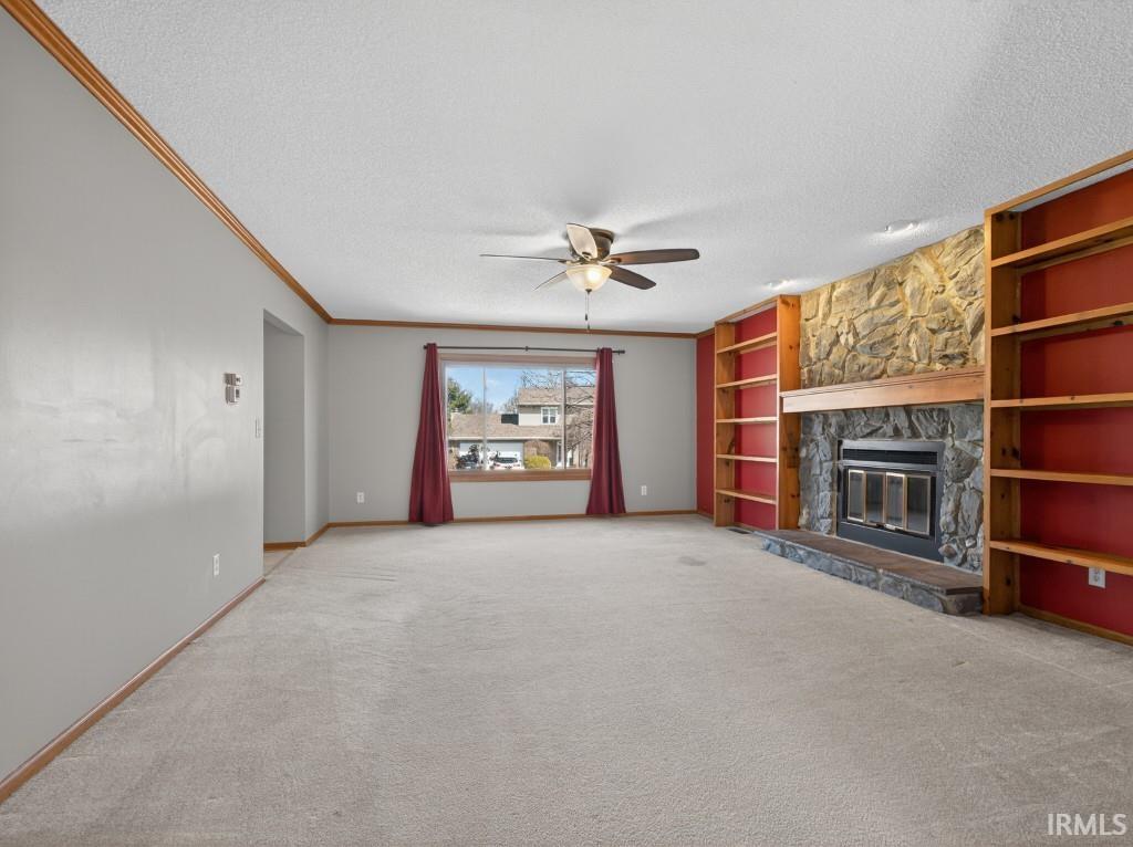 Unfurnished living room featuring a textured ceiling, built in features, a stone fireplace, carpet floors, and a ceiling fan