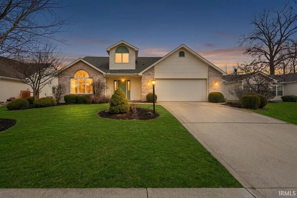 Traditional-style home featuring an attached garage, concrete driveway, a front lawn, and brick siding