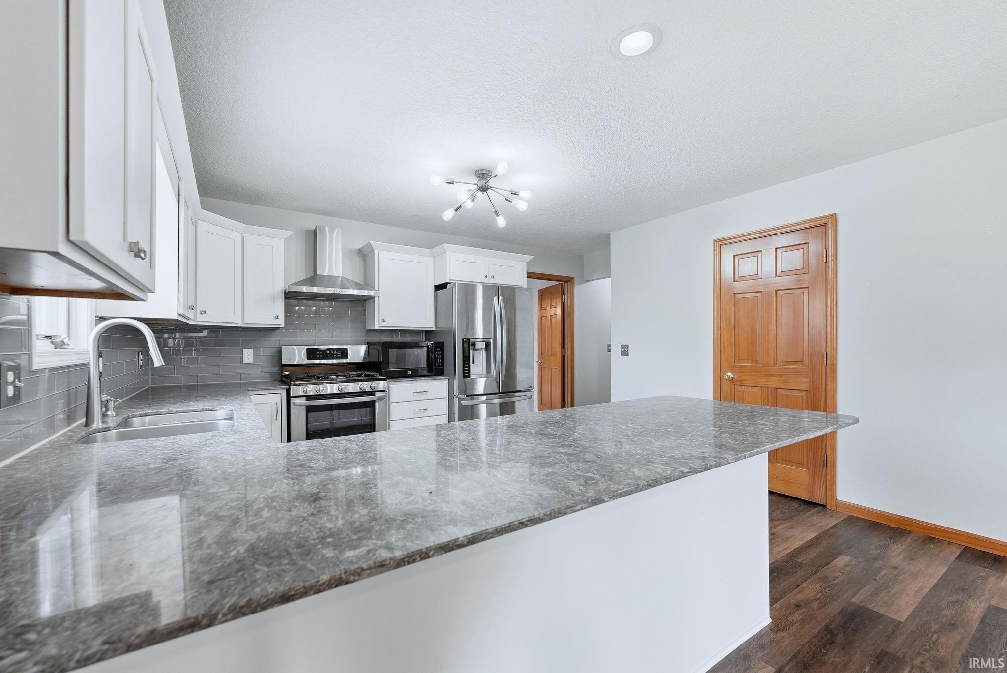 Kitchen featuring stainless steel appliances, dark stone counters, white cabinetry, tasteful backsplash, and a peninsula