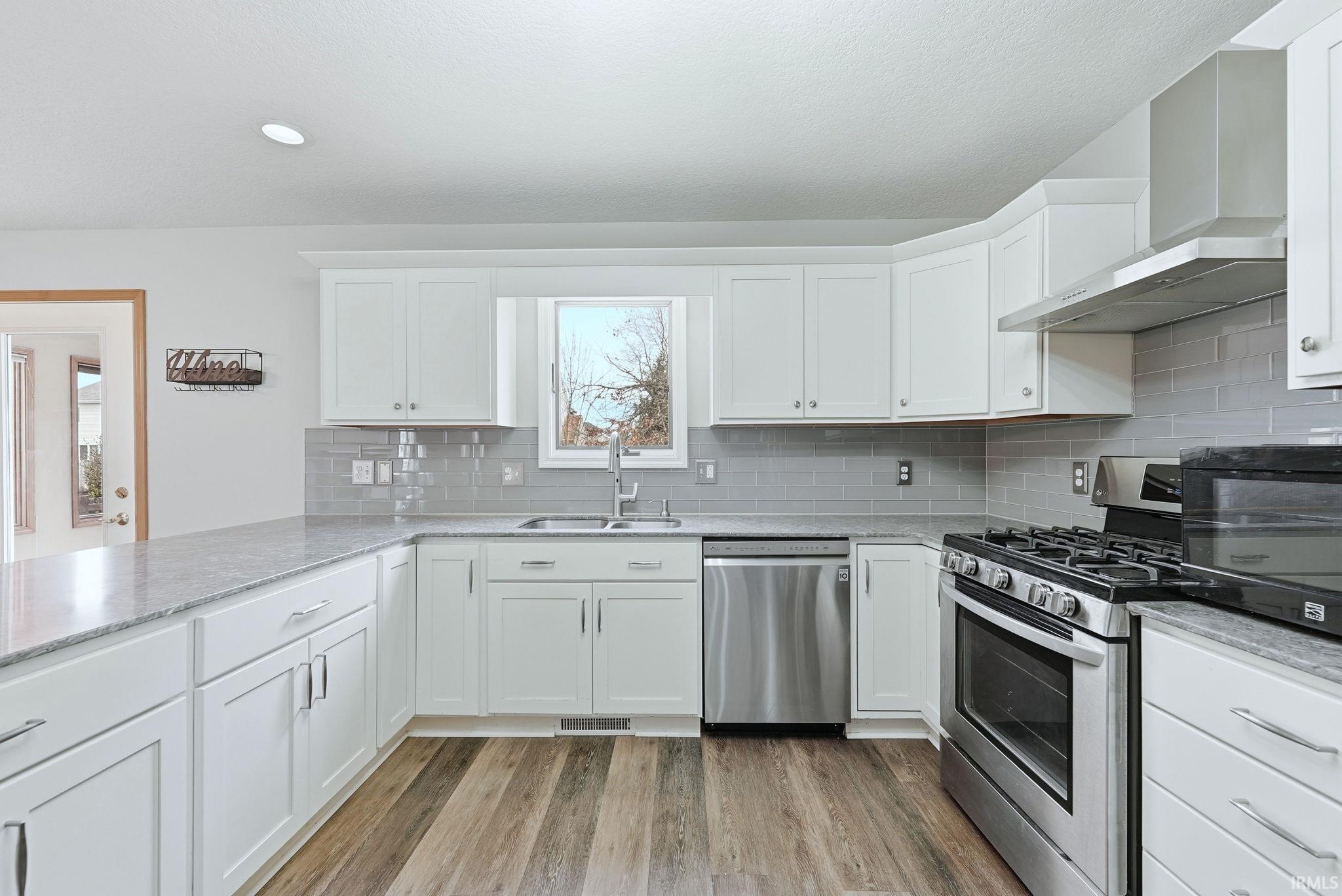 Kitchen featuring white cabinets, stainless steel appliances, light wood-style floors, and light stone counters