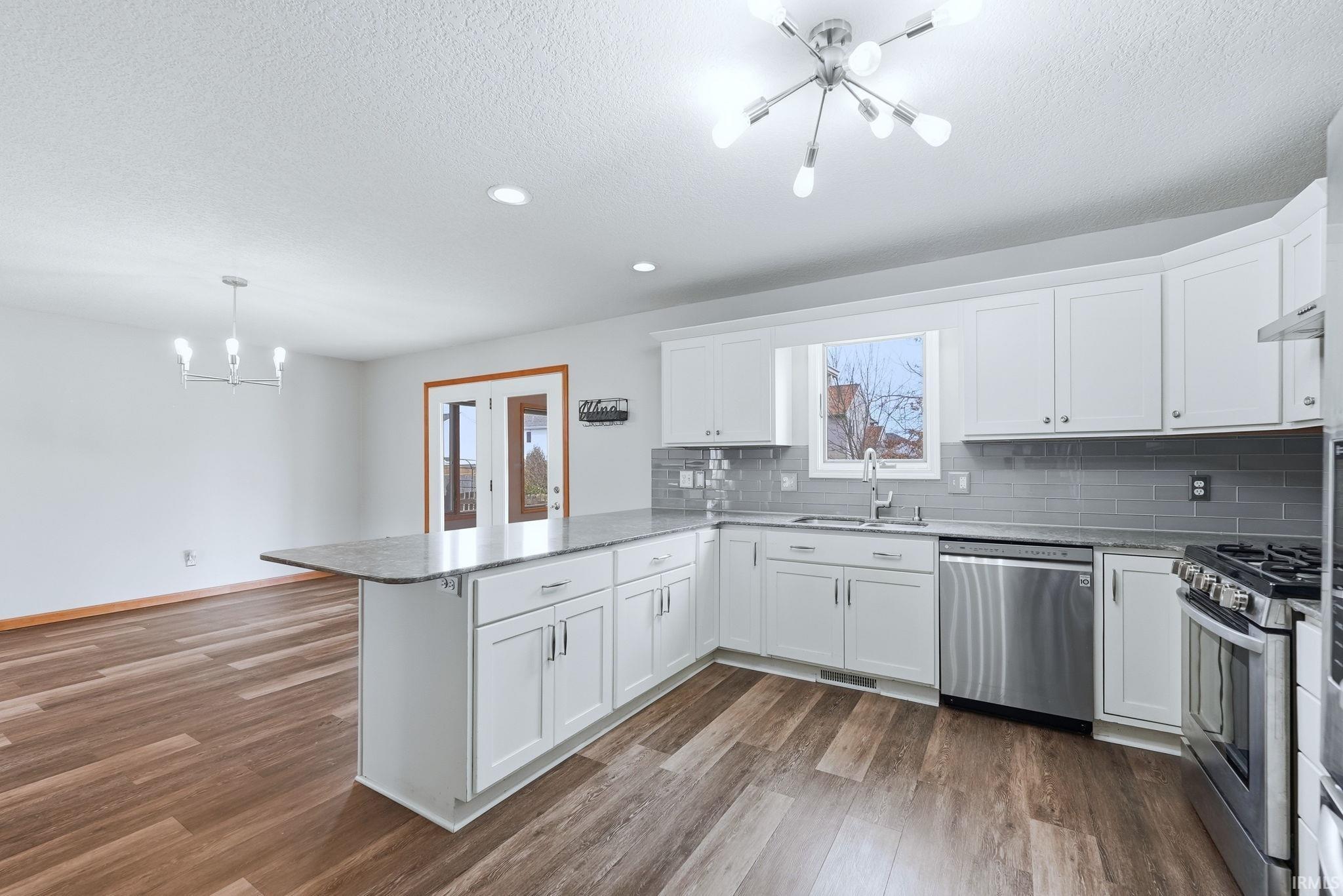 Kitchen with suspended lighting, white cabinets, a peninsula, stainless steel appliances, and dark wood-style floors