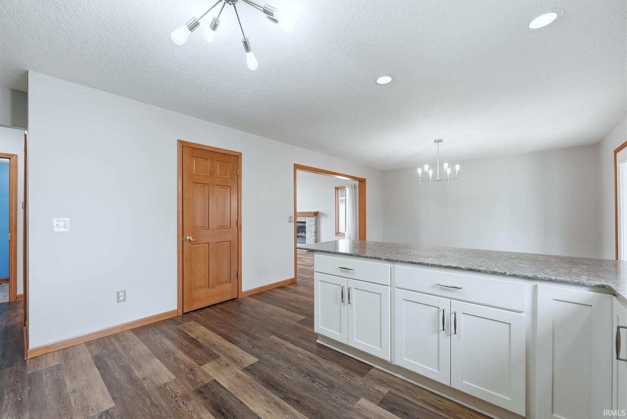 Kitchen featuring white cabinetry, a chandelier, dark wood-style floors, light stone countertops, and a textured ceiling