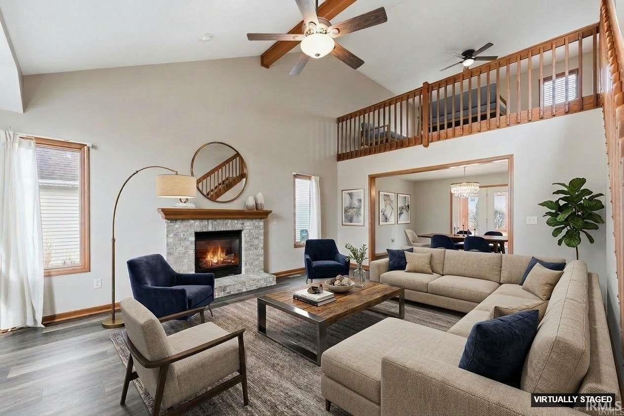 Living room featuring ceiling fan, wood finished floors, a stone fireplace, a high ceiling, and hanging lights