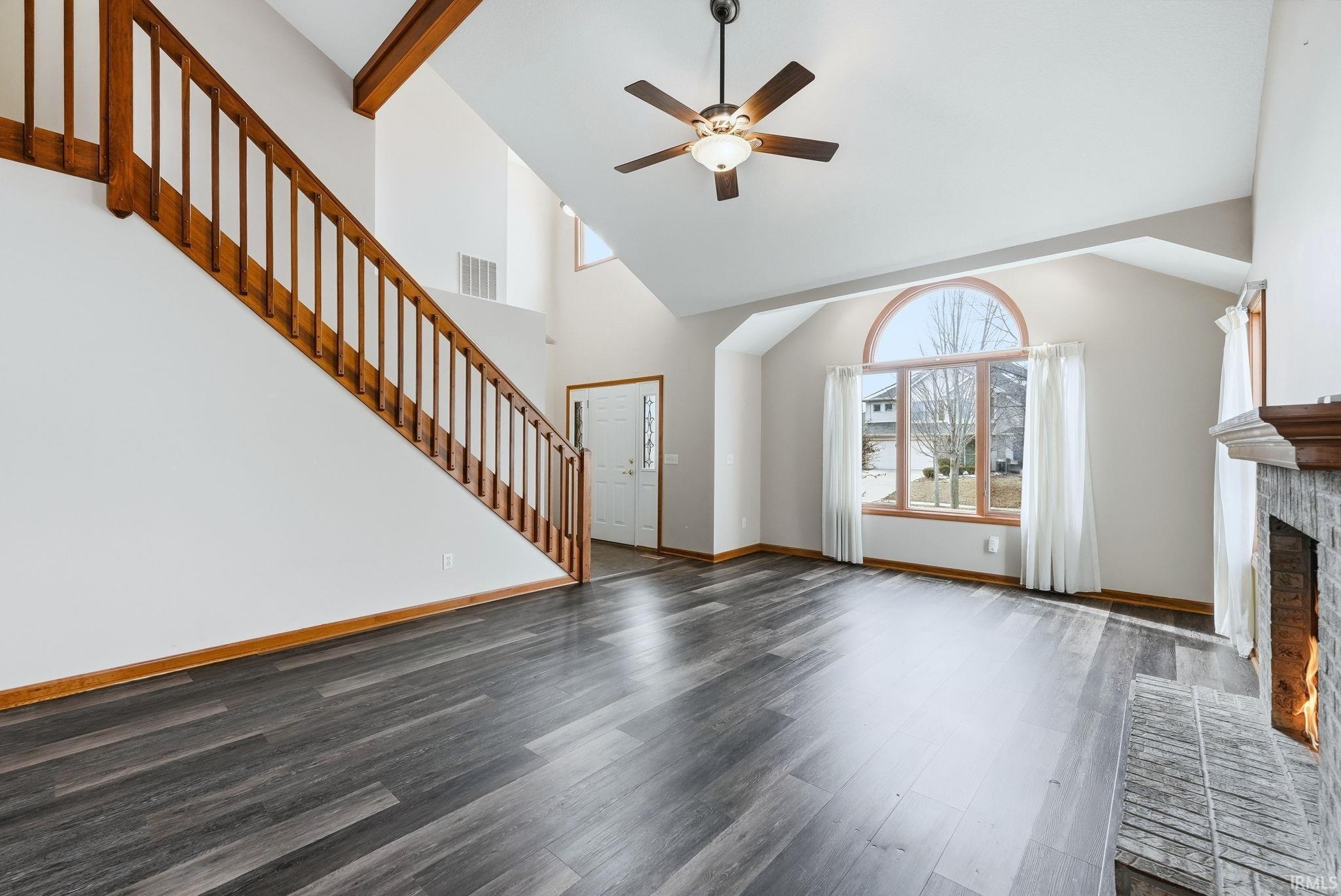 Unfurnished living room with a ceiling fan, lofted ceiling, dark wood-style floors, and a brick fireplace
