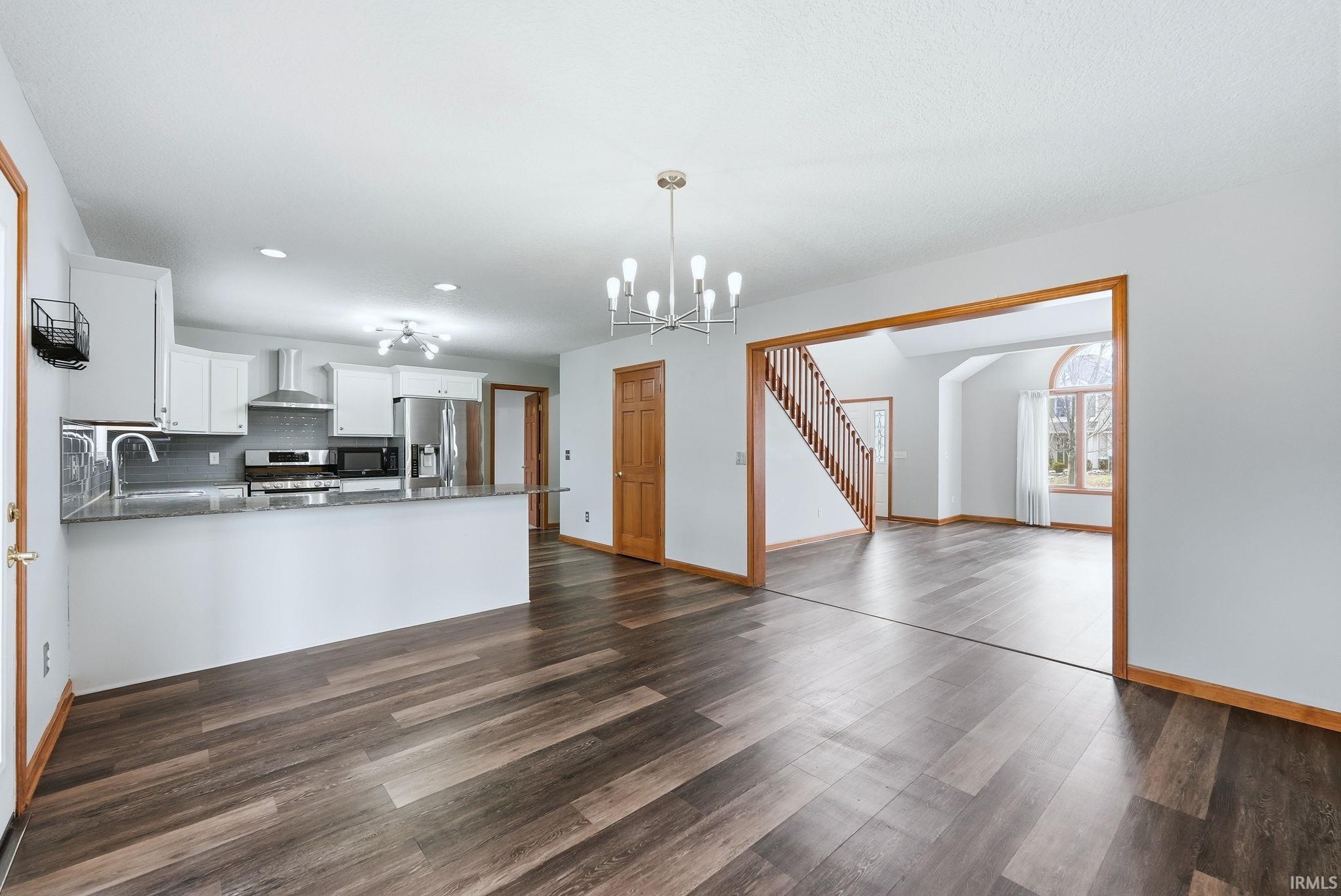 Kitchen with white cabinetry, dark stone countertops, stainless steel appliances, suspended lighting, and decorative backsplash