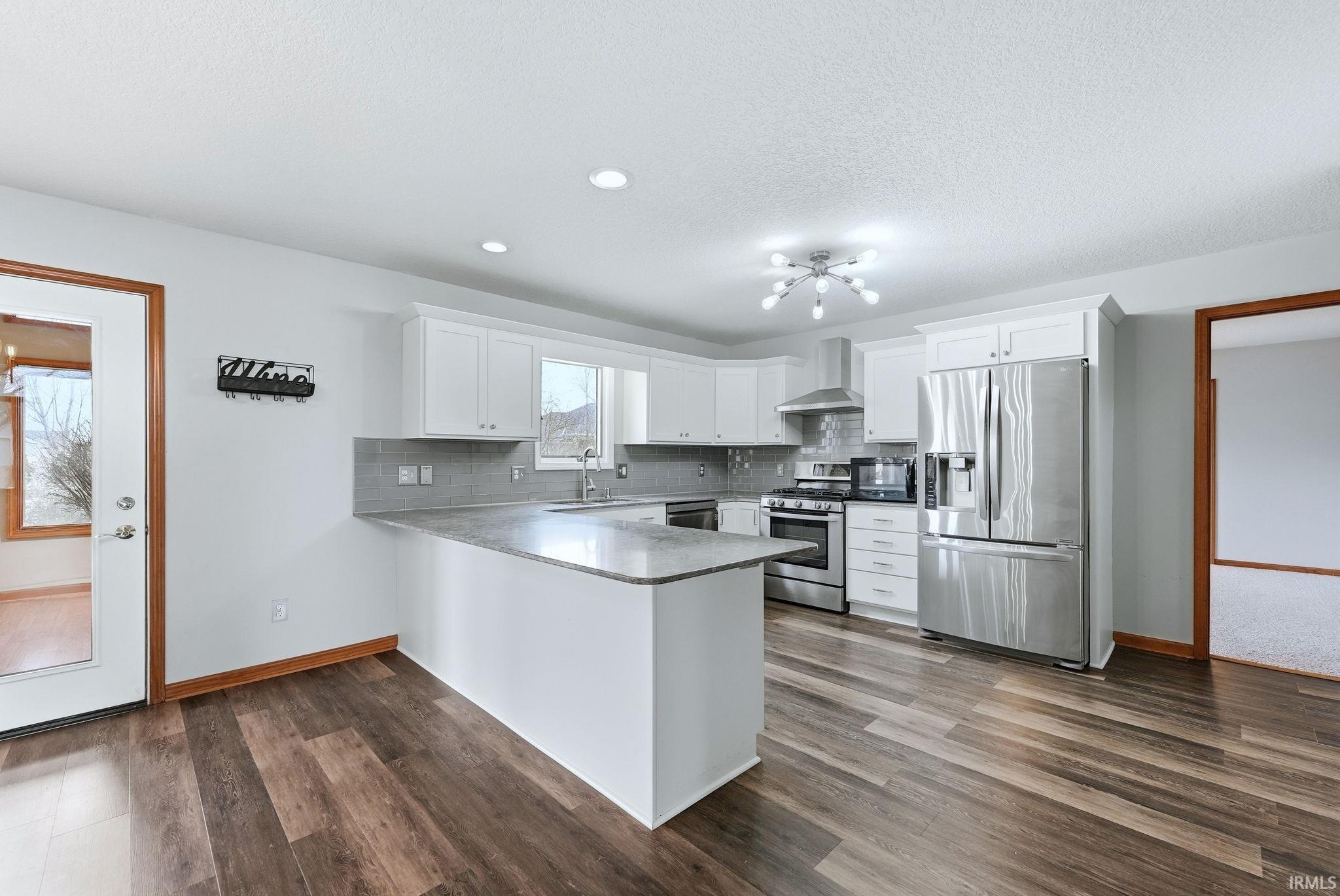 Kitchen featuring stainless steel appliances, white cabinetry, a peninsula, backsplash, and recessed lighting
