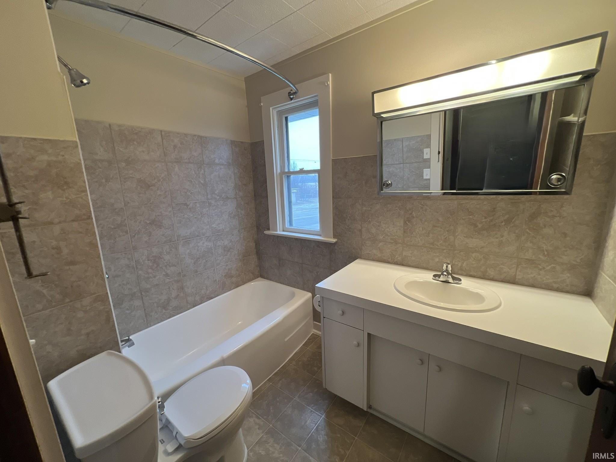 Bathroom with tile walls, vanity, shower / bathtub combination, a wainscoted wall, and dark tile patterned floors