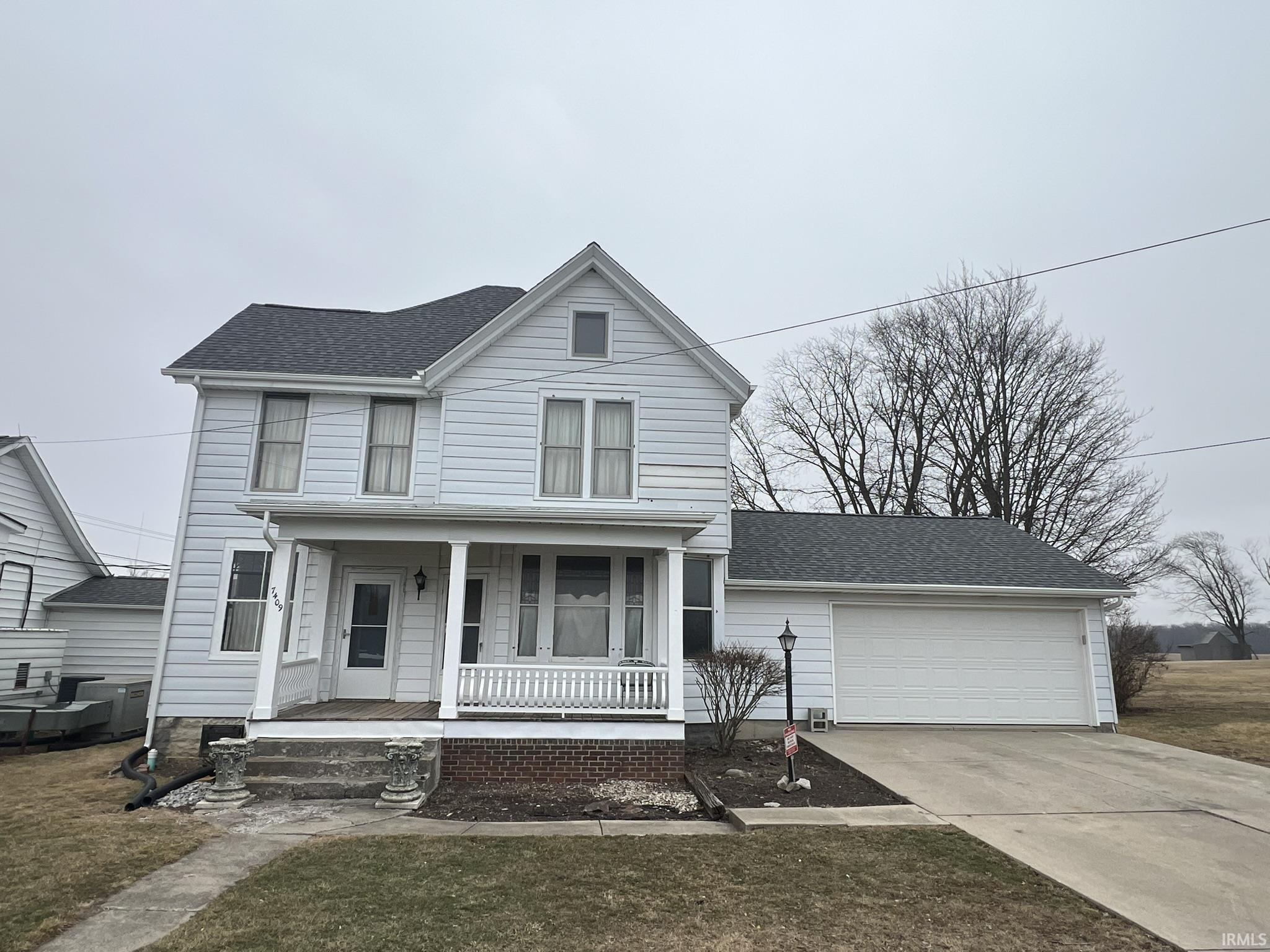 Traditional-style house with a porch, concrete driveway, a shingled roof, an attached garage, and a front yard