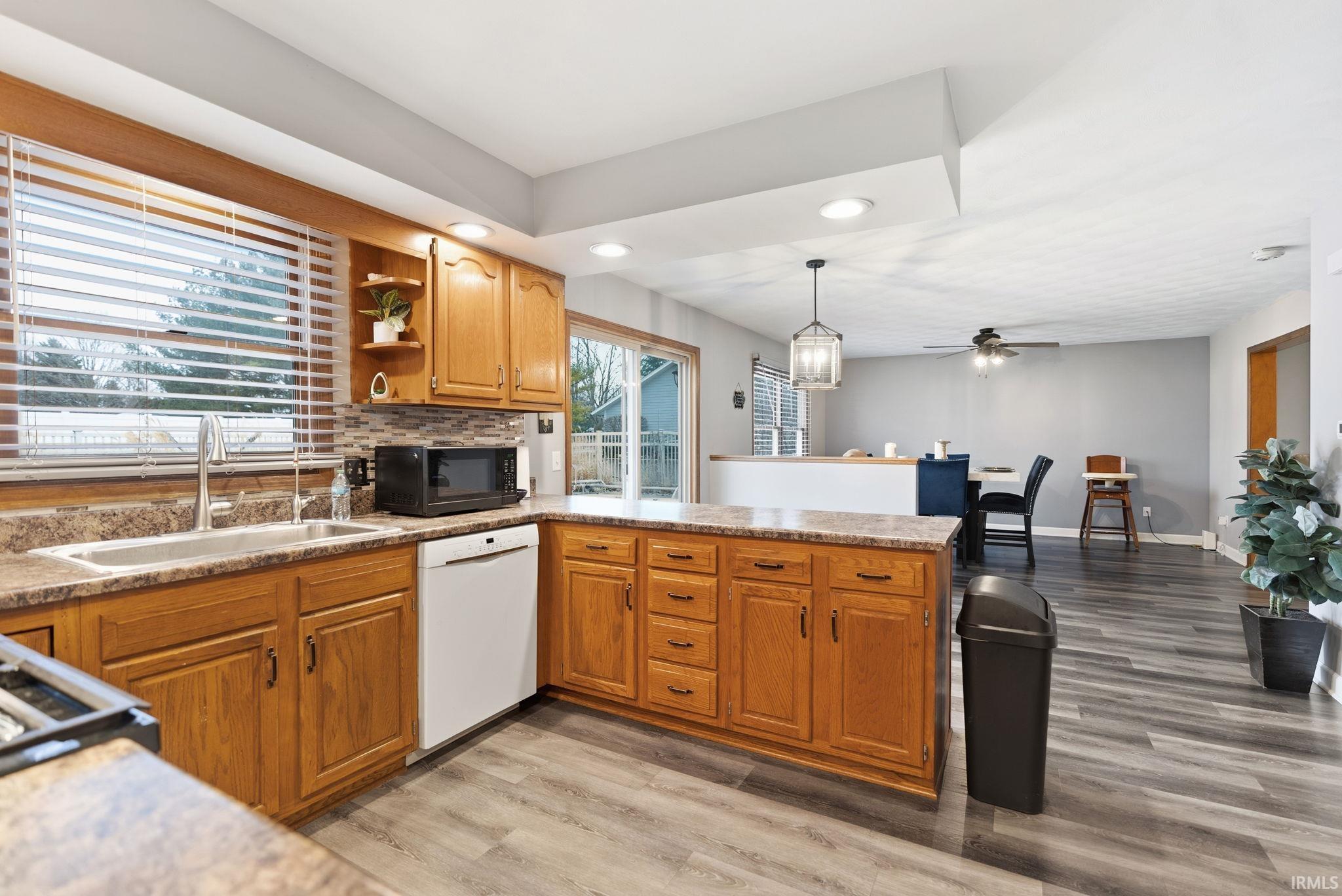 Kitchen with tasteful backsplash, pendant lighting, open shelves, dishwasher, and light wood-style flooring
