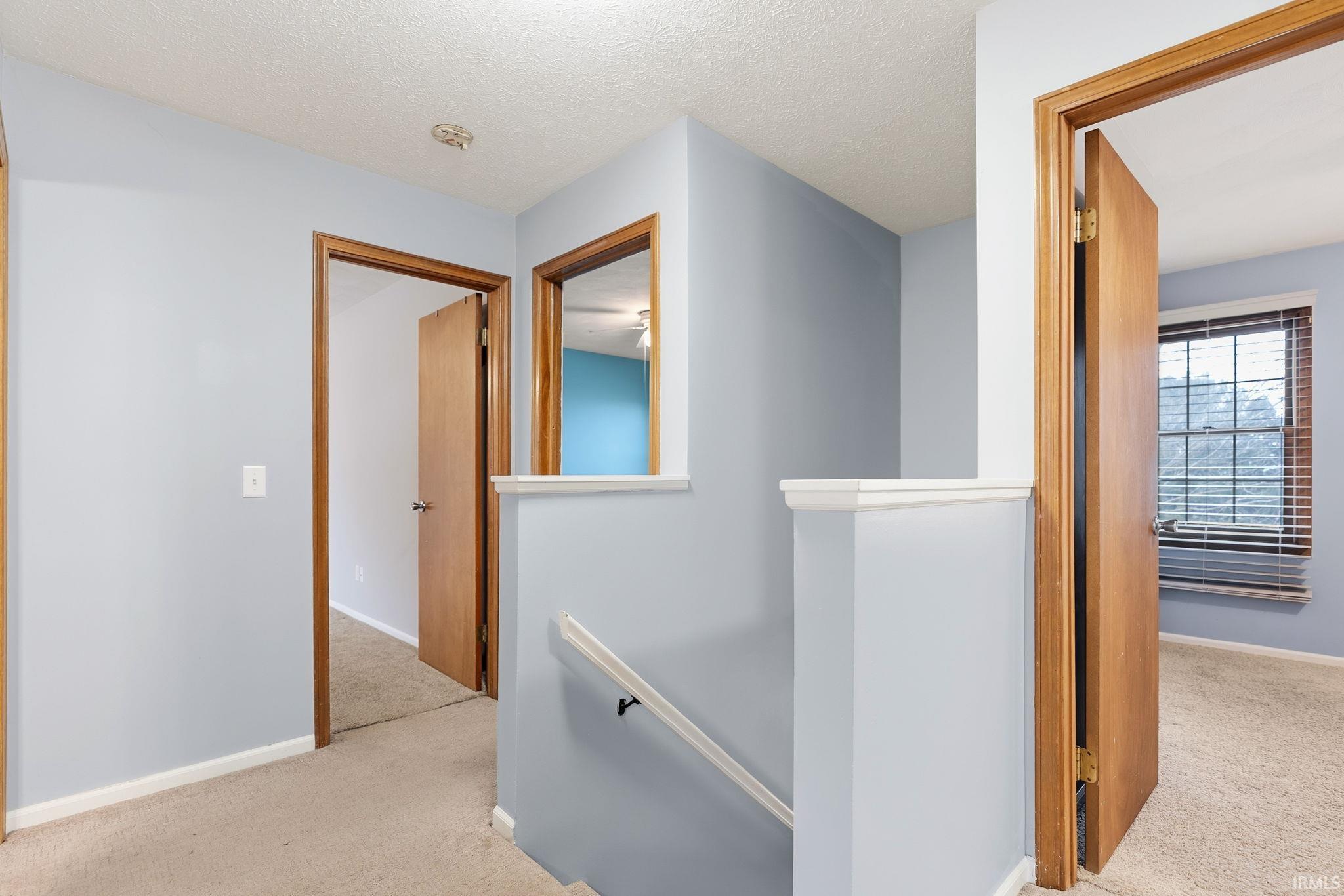 Hall with an upstairs landing, light carpet, and a textured ceiling