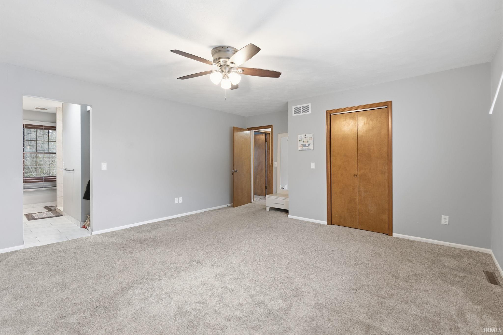 Unfurnished bedroom with a closet, light colored carpet, a ceiling fan, and ensuite bath