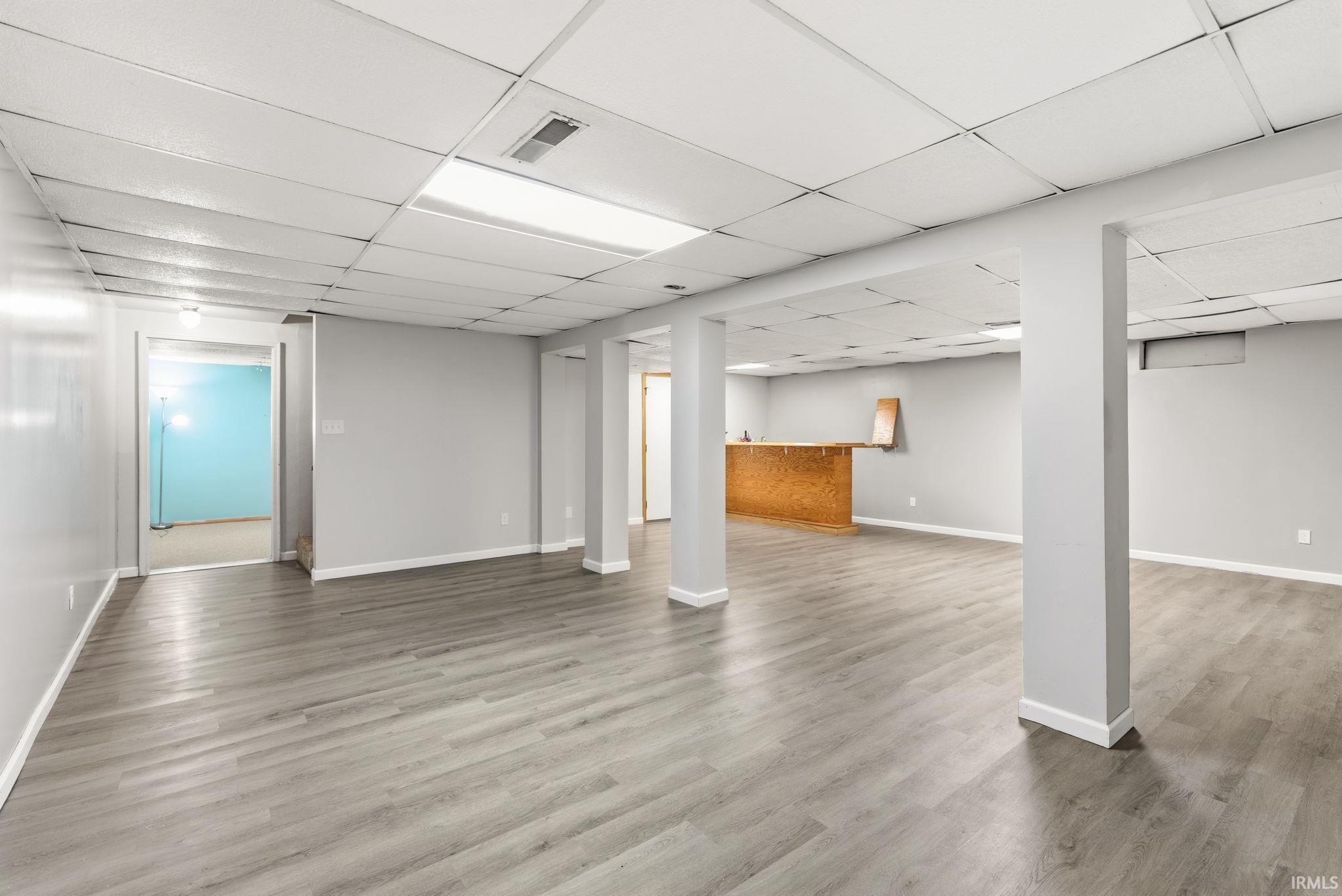 Finished basement featuring a drop ceiling, light wood-type flooring, and bar area