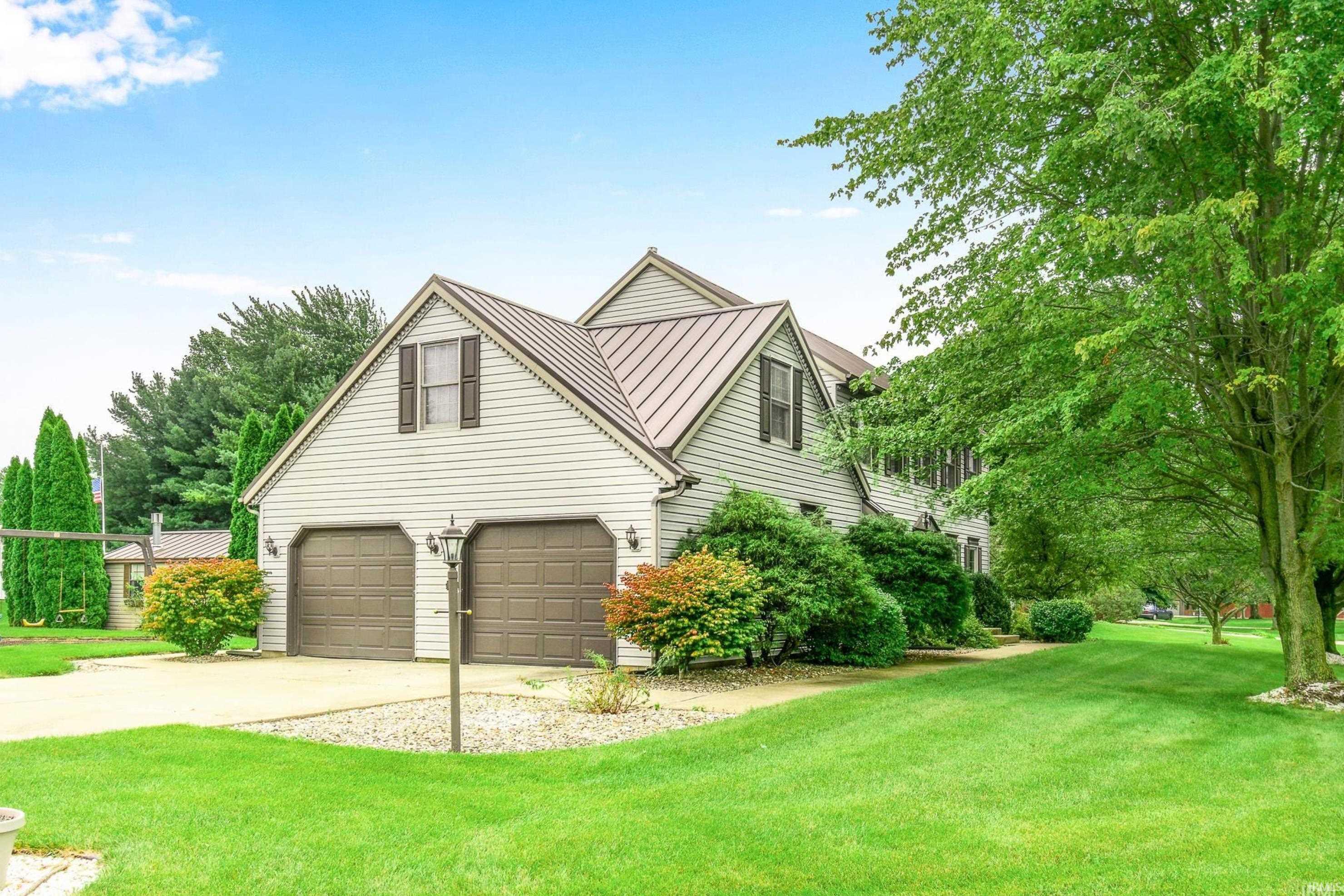 View of front of property featuring a standing seam roof, driveway, a front lawn, and a garage