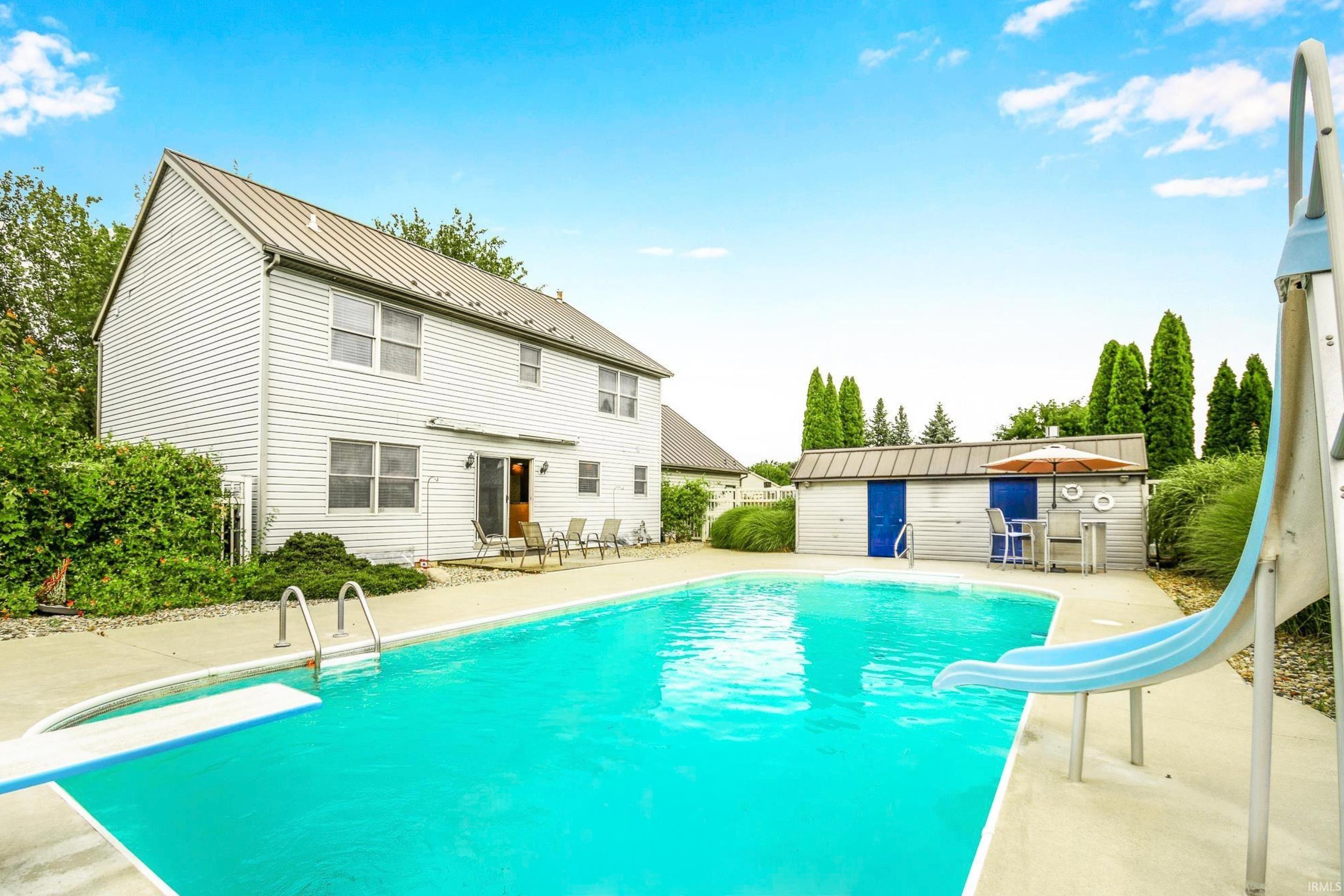 Outdoor pool with a patio area, a water slide, a diving board, and an outbuilding