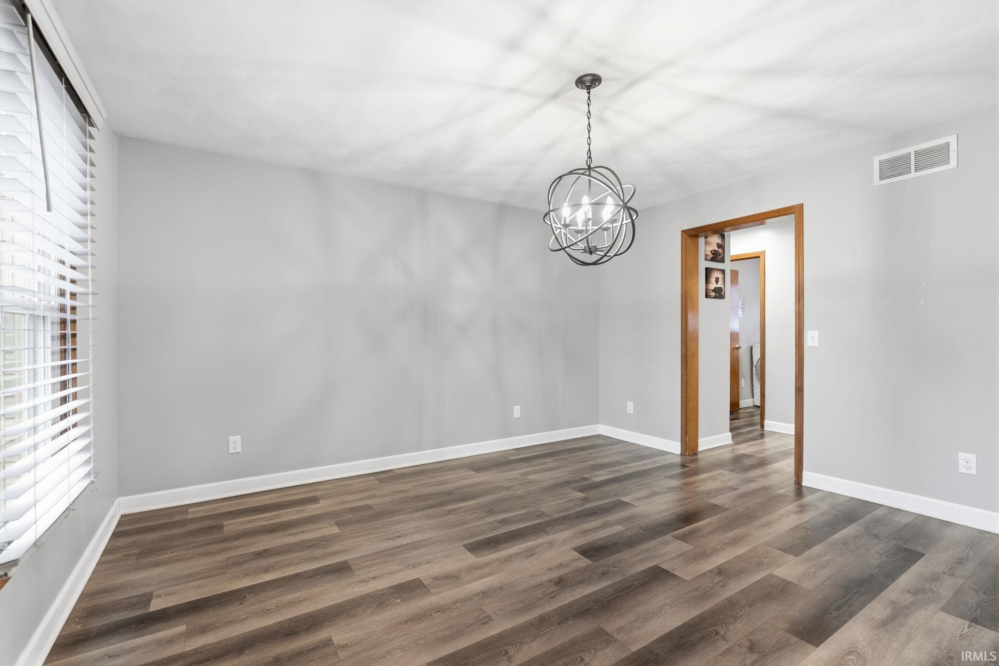 Spare room featuring a chandelier and dark wood-style flooring