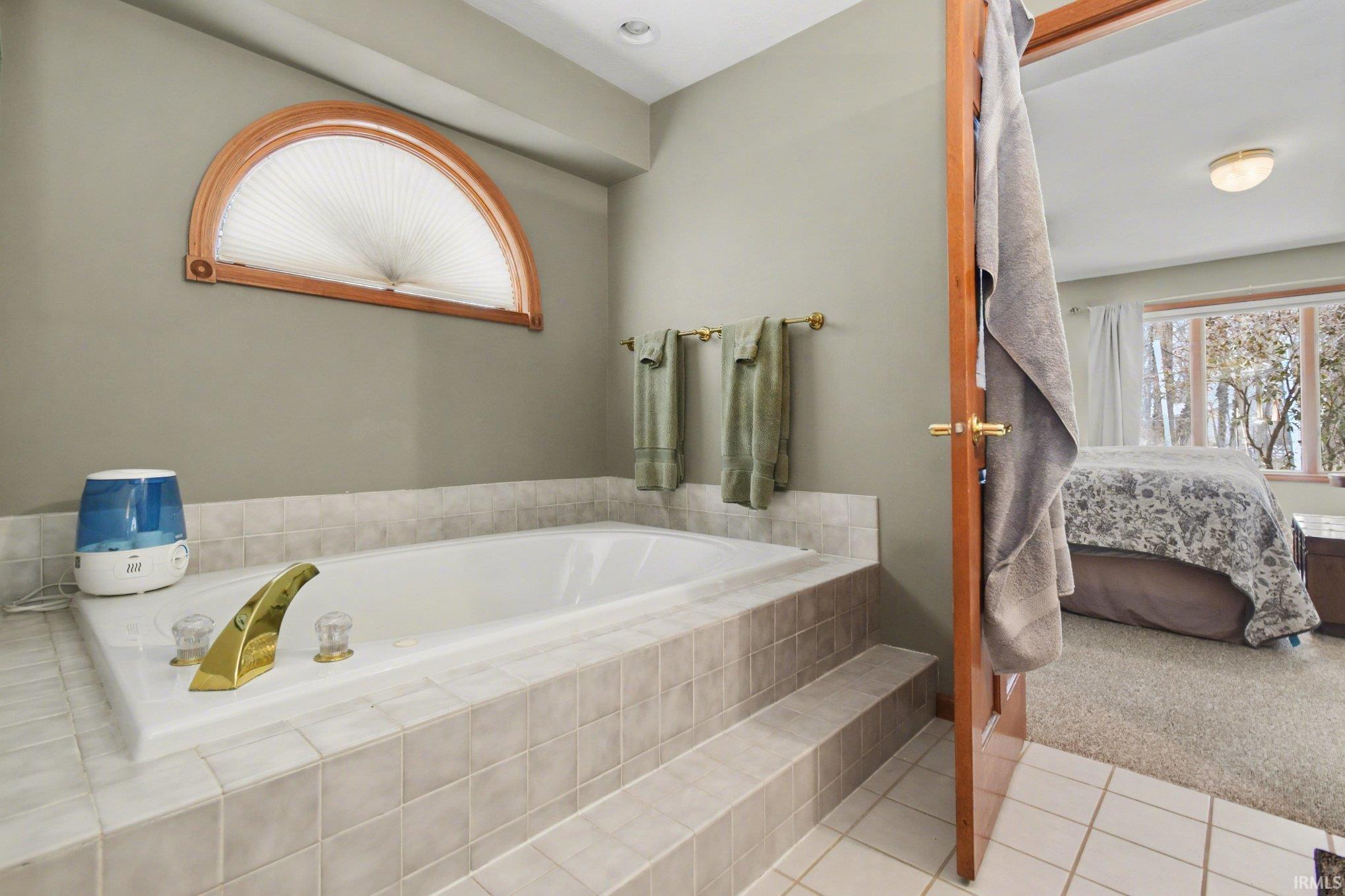 Full bathroom featuring a bath, ensuite bathroom, light tile patterned floors, and light colored carpet