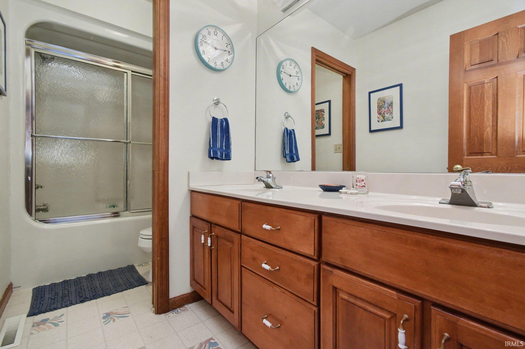 Full bath with double vanity and bath / shower combo with glass door