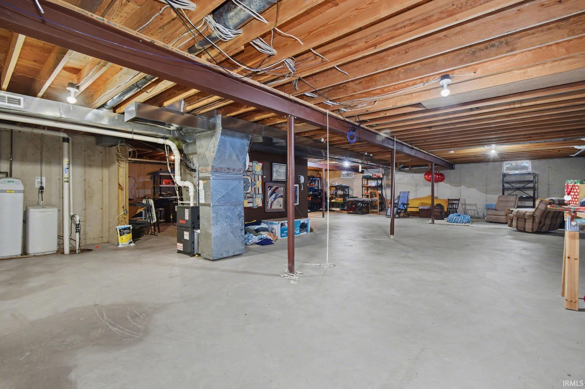 Unfinished basement with a water softener, heating unit, and drainage system