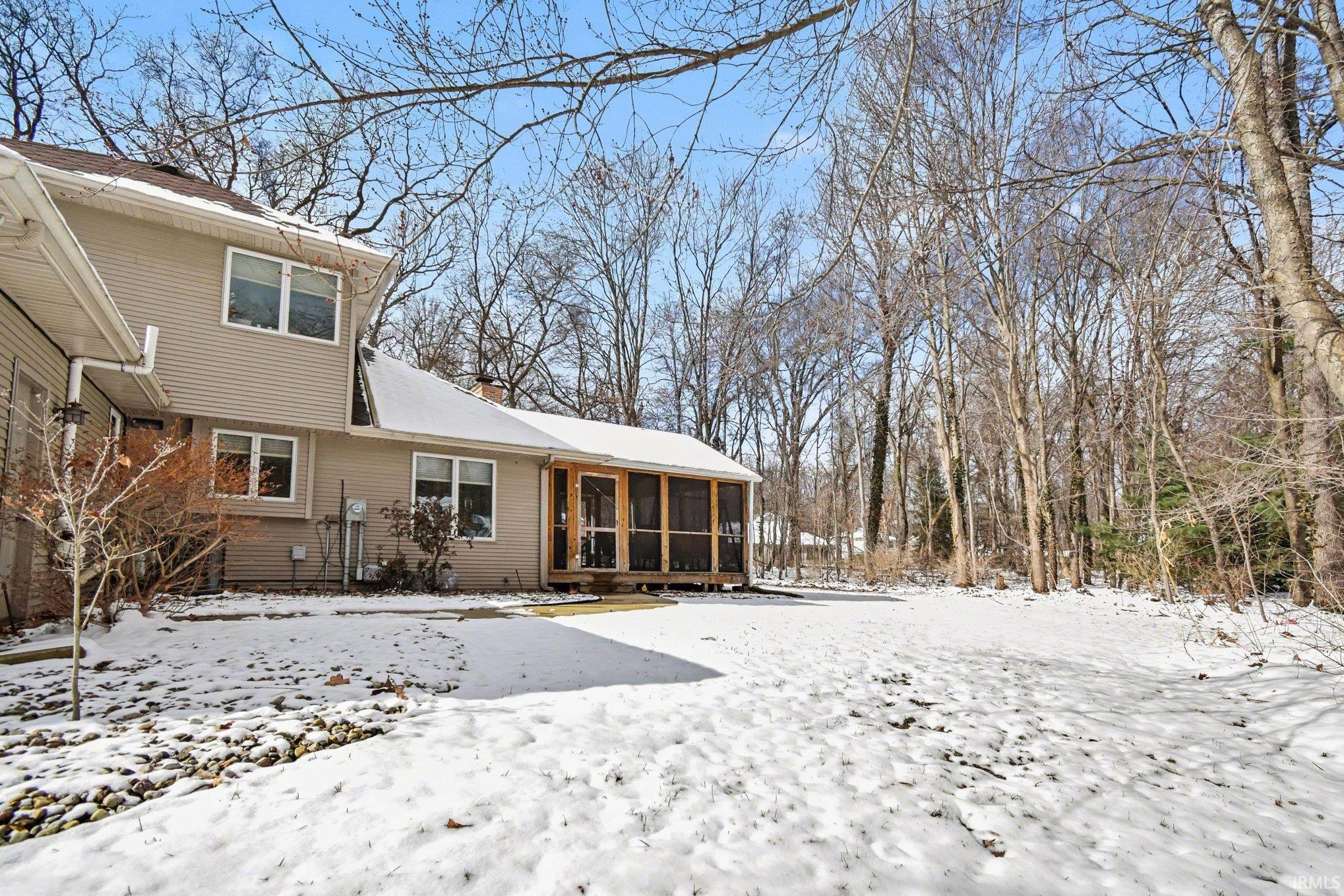 Snow covered back of property with a sunroom and a chimney
