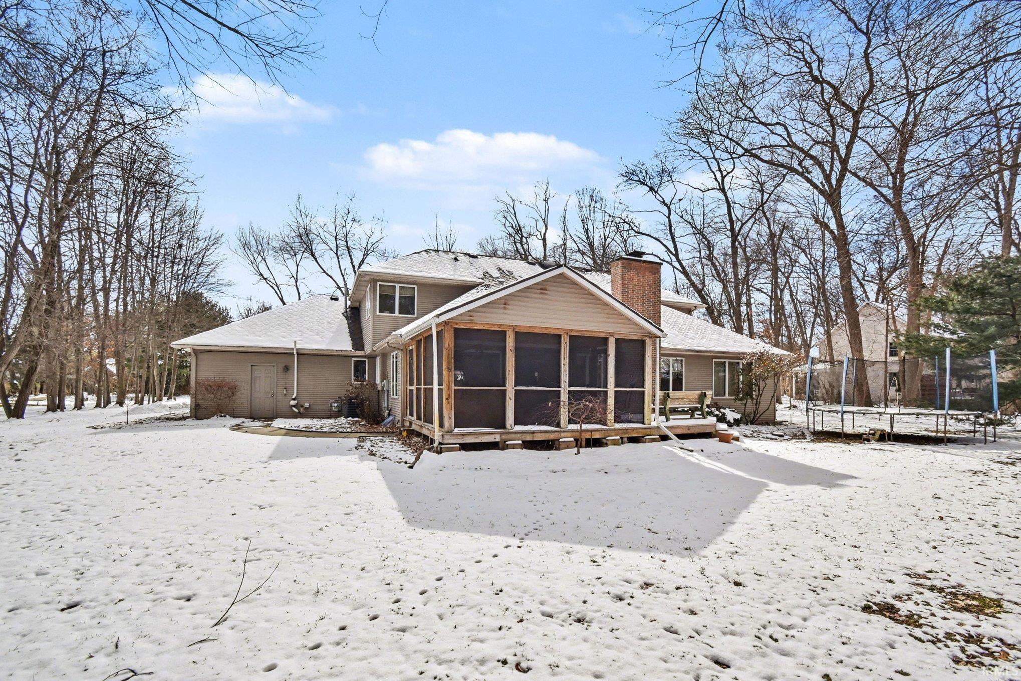 Snow covered rear of property with a trampoline, a sunroom, and a chimney