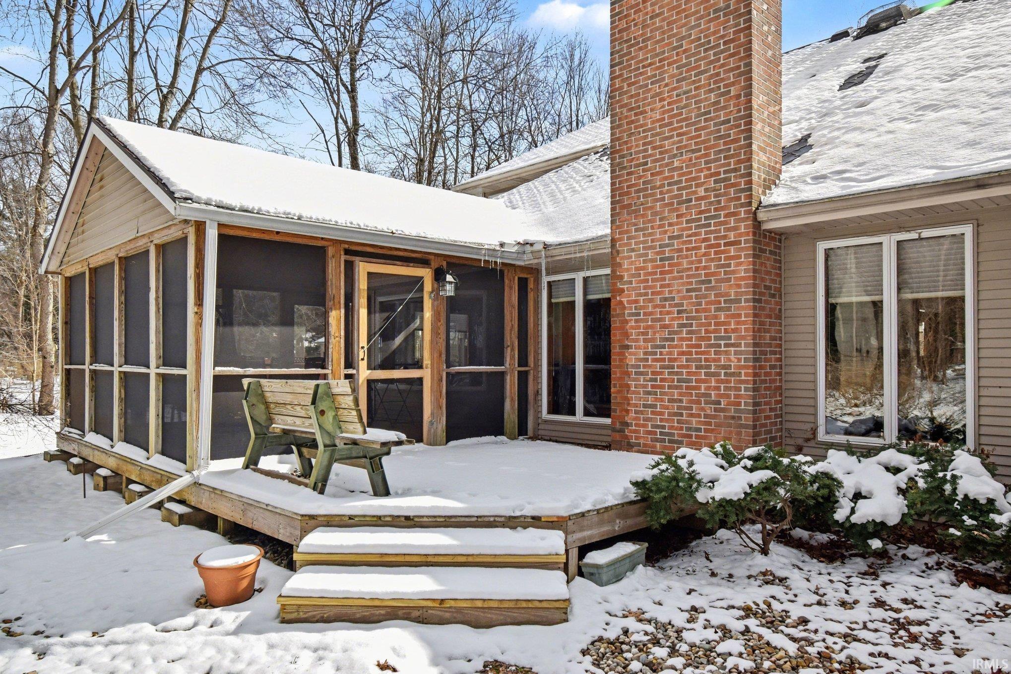 Snow covered back of property featuring a chimney, a wooden deck, and a sunroom