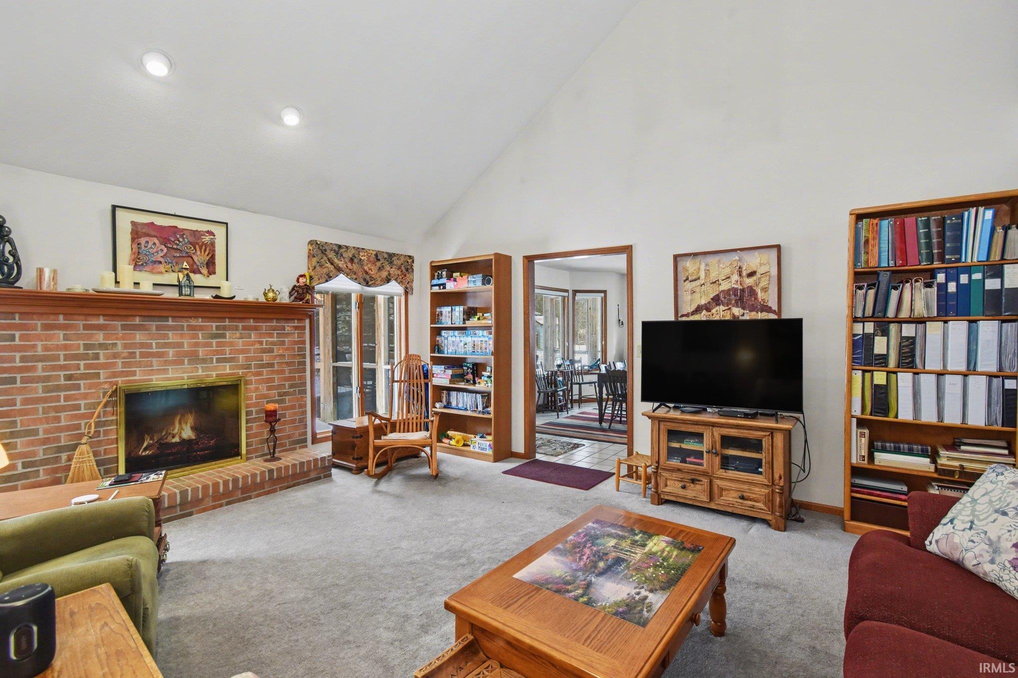 Living room with carpet, lofted ceiling, and a brick fireplace