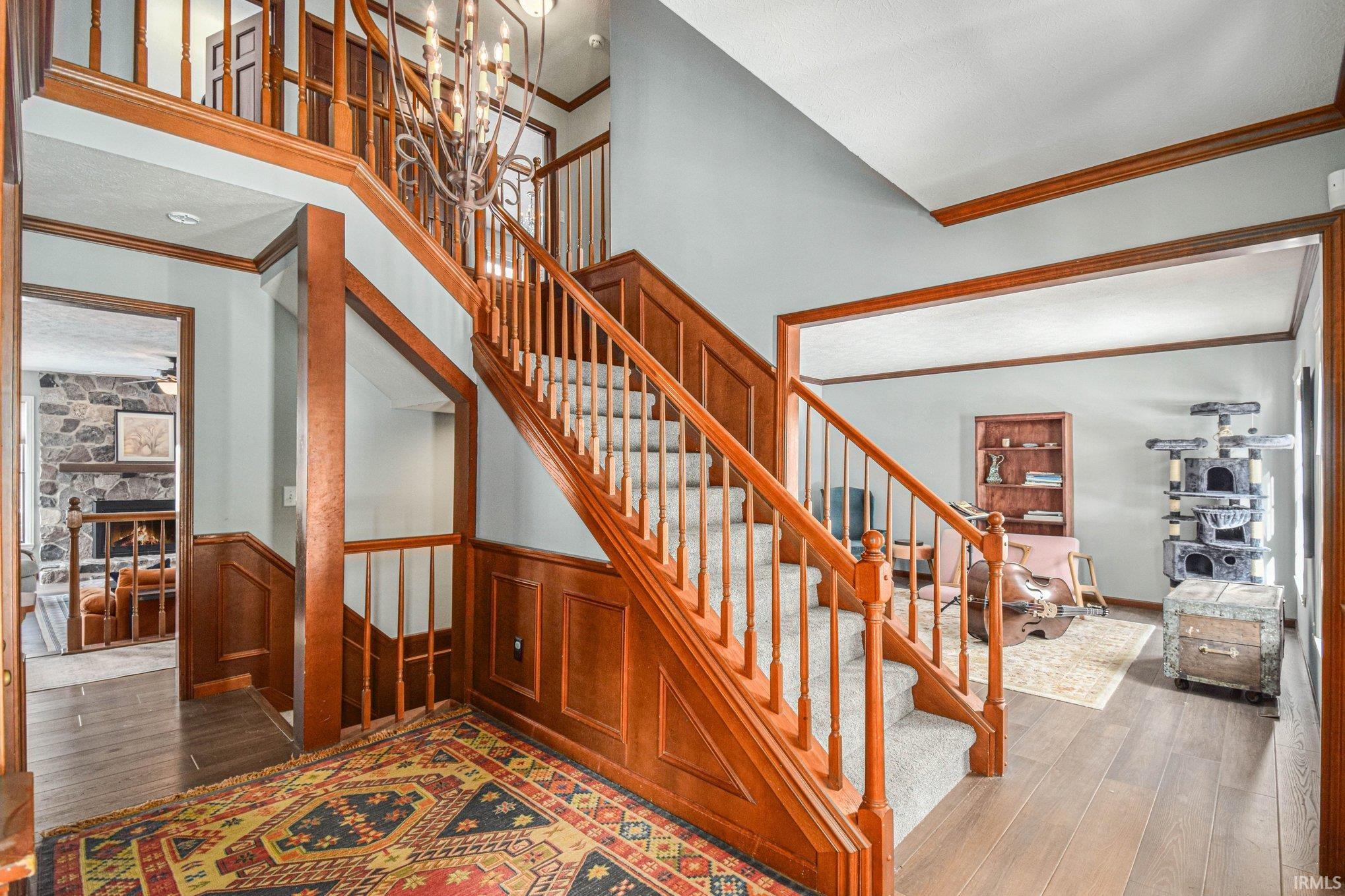 Stairs with ornamental molding, hardwood / wood-style floors, a stone fireplace, a wainscoted wall, and a high ceiling