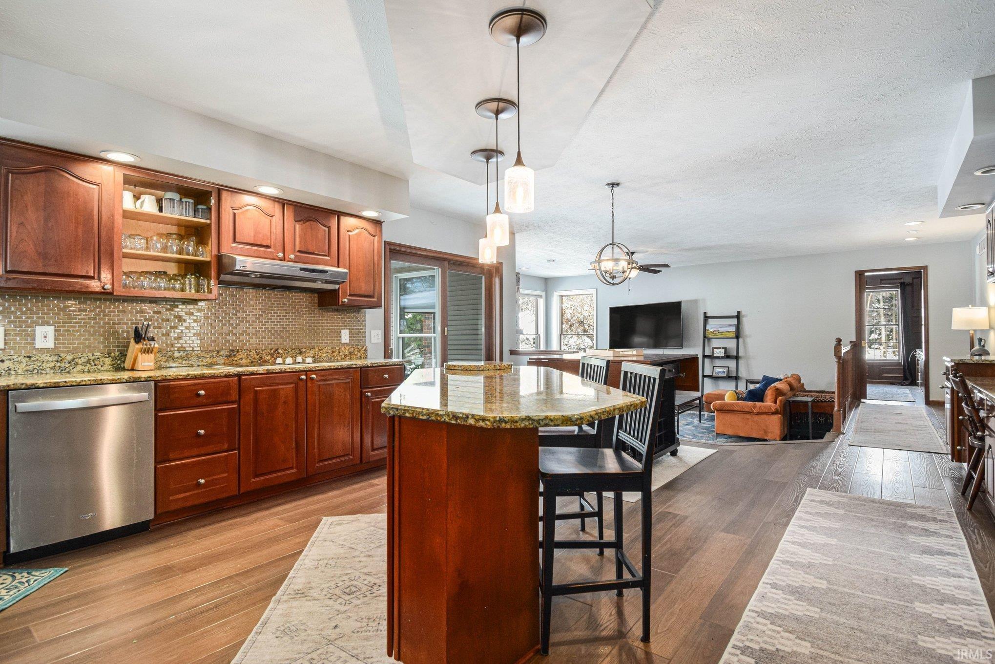 Kitchen with stainless steel dishwasher, a kitchen breakfast bar, light stone countertops, open floor plan, and dark wood finished floors