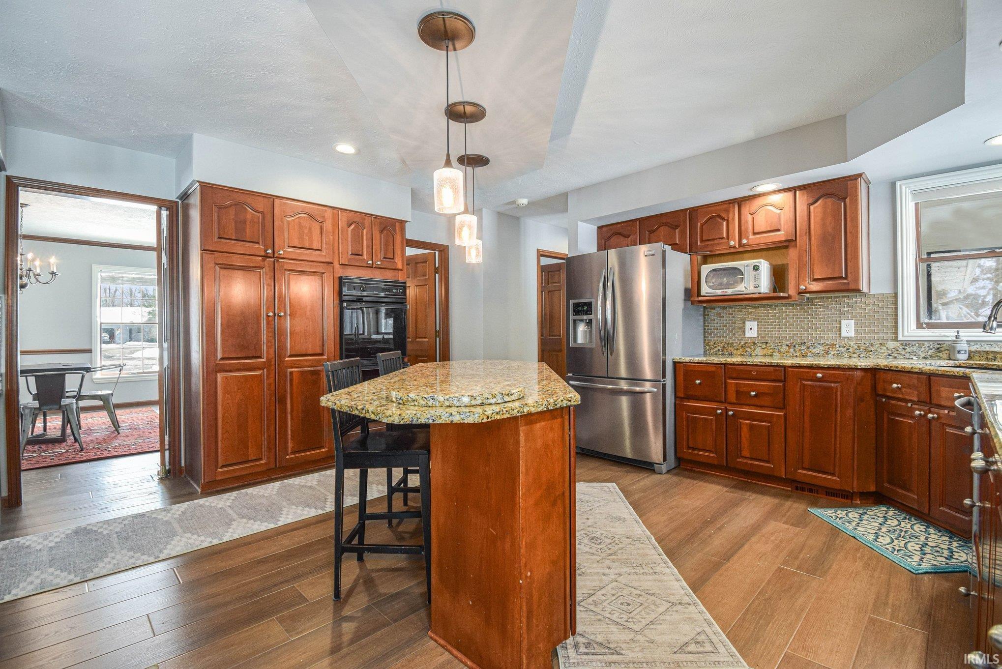Kitchen featuring stainless steel refrigerator with ice dispenser, light stone countertops, a kitchen island, wood finish cabinets, and black oven