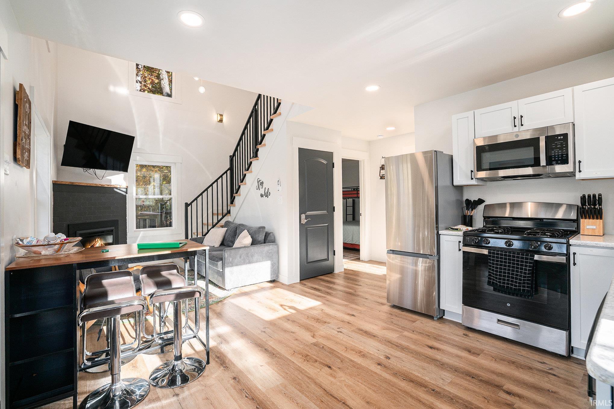 Kitchen featuring stainless steel appliances, a warm lit fireplace, light wood-style flooring, open floor plan, and white cabinets