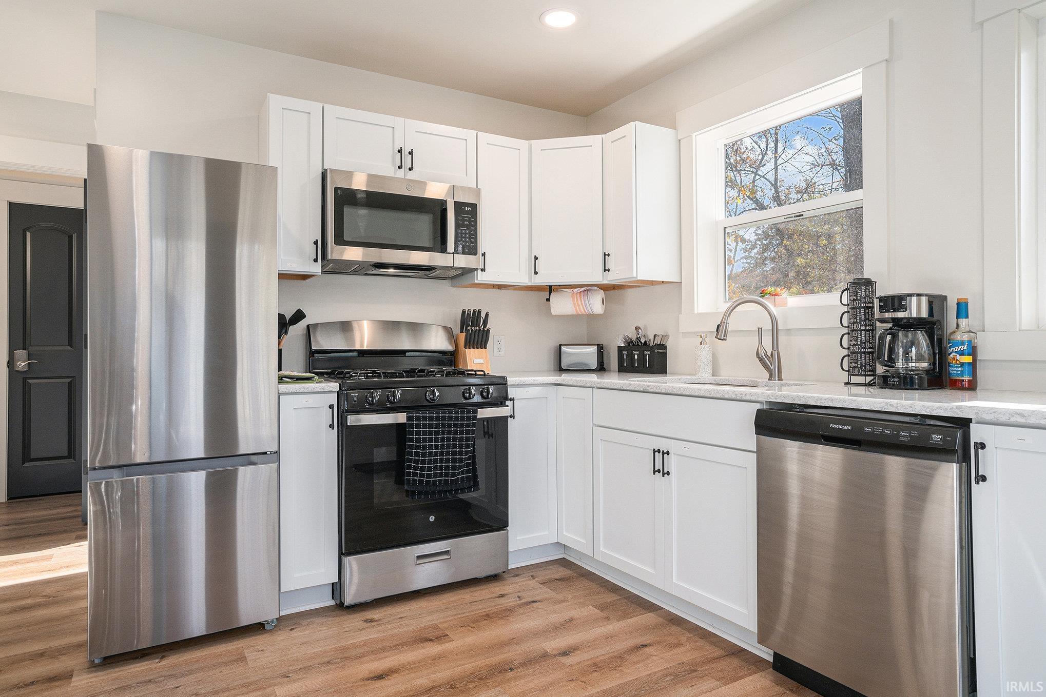 Kitchen with stainless steel appliances, white cabinetry, light wood-style floors, light stone countertops, and recessed lighting