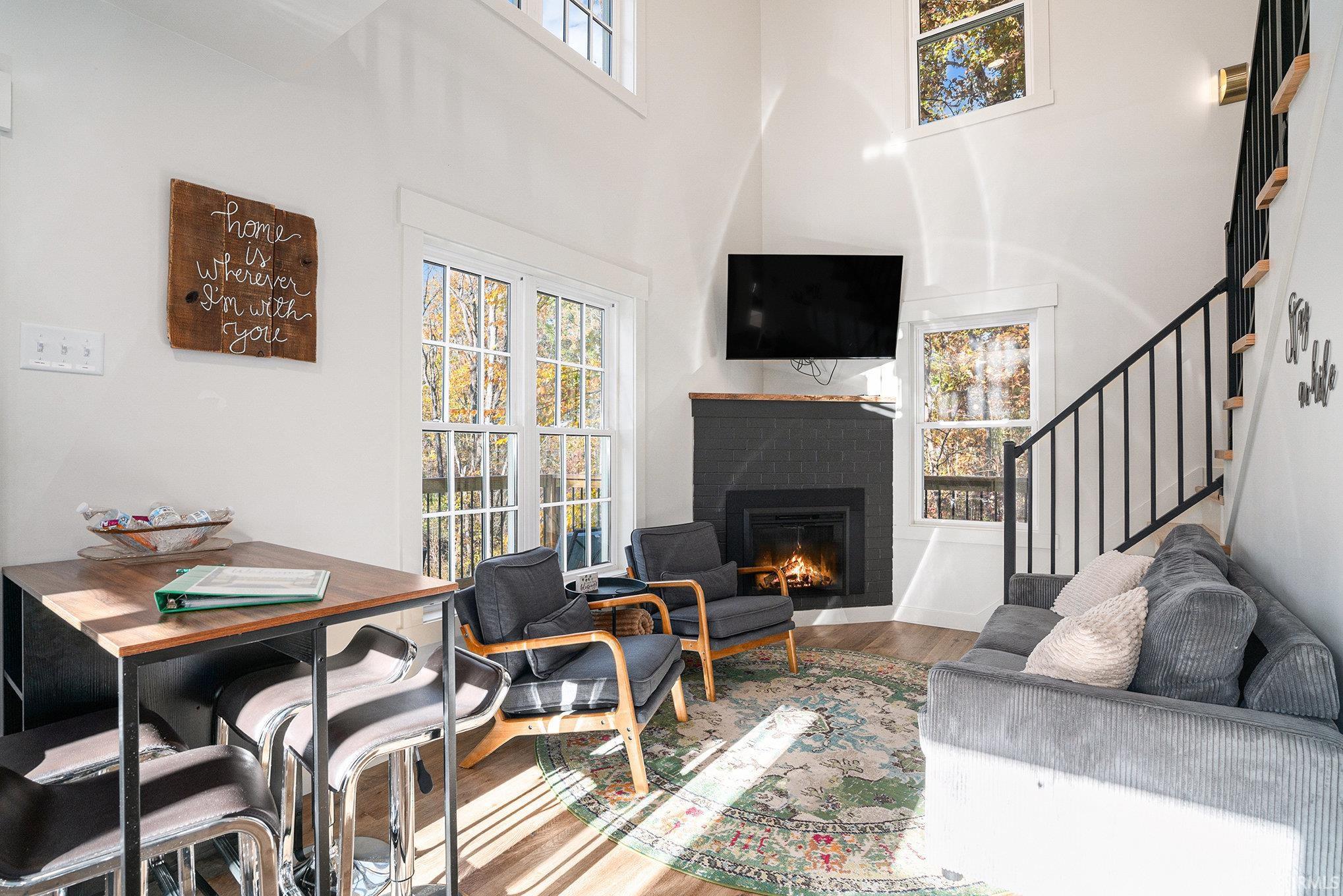 Living area featuring a fireplace, plenty of natural light, wood finished floors, and a high ceiling