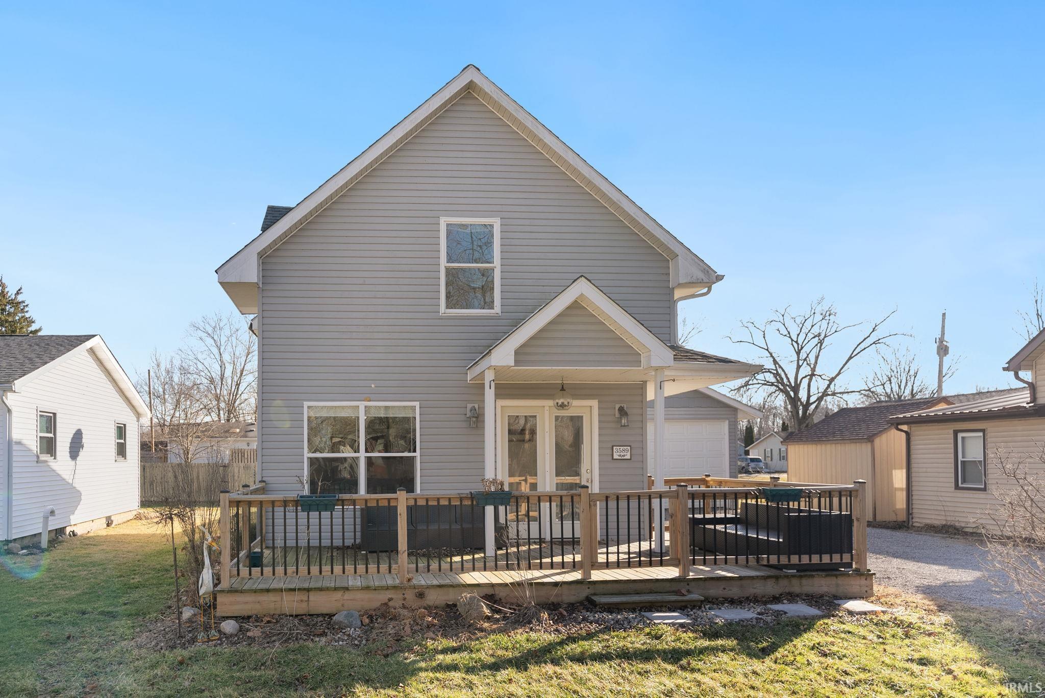 Rear view of house with a wooden deck, a lawn, and a garage