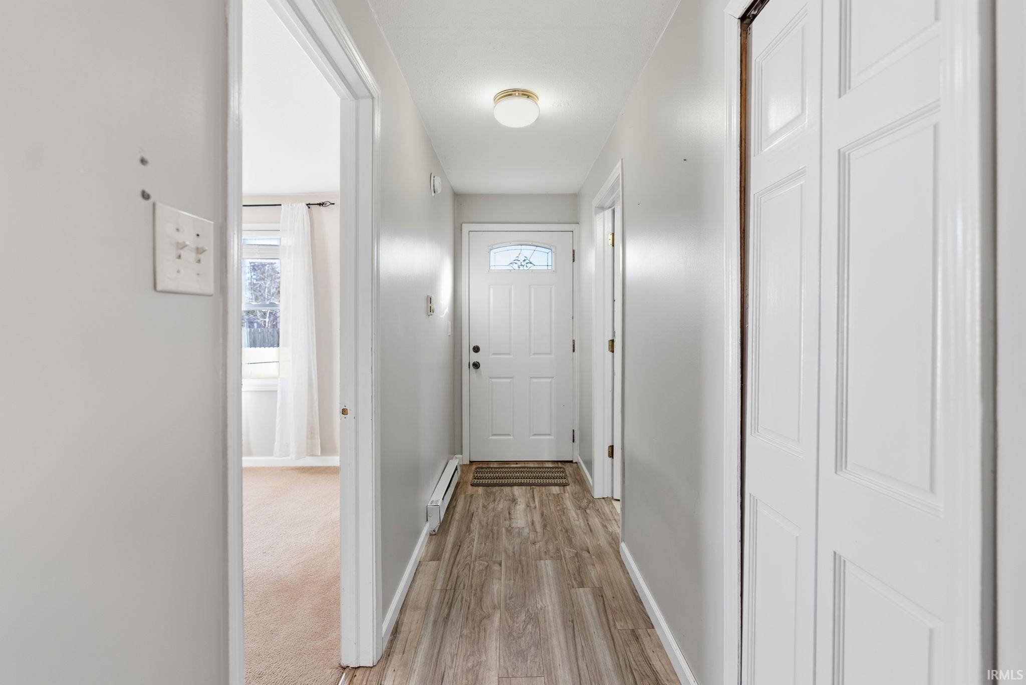 Hall featuring light wood-style flooring, healthy amount of natural light, and a baseboard heating unit