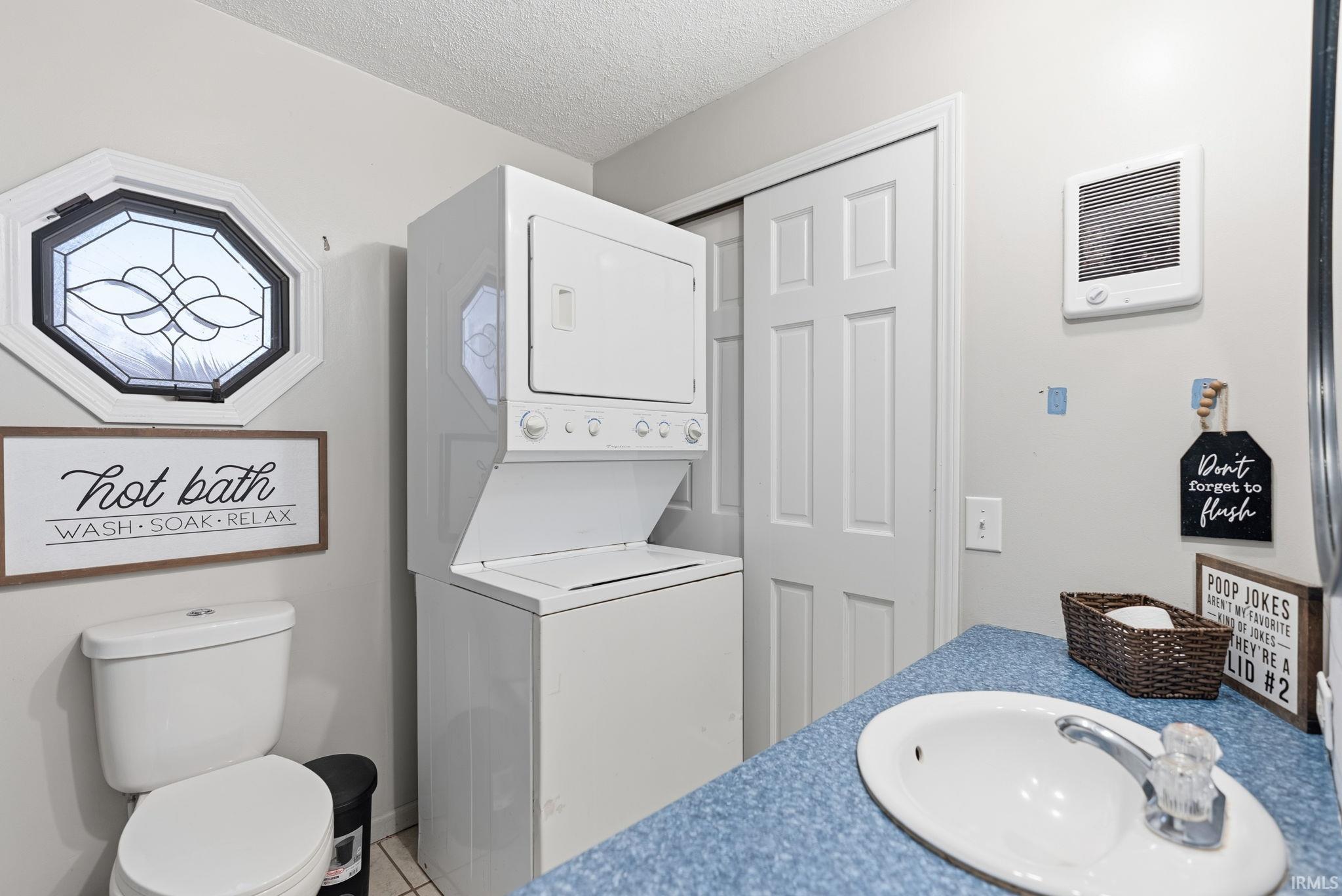 Bathroom with vanity, stacked washer and dryer, a textured ceiling, and heating unit