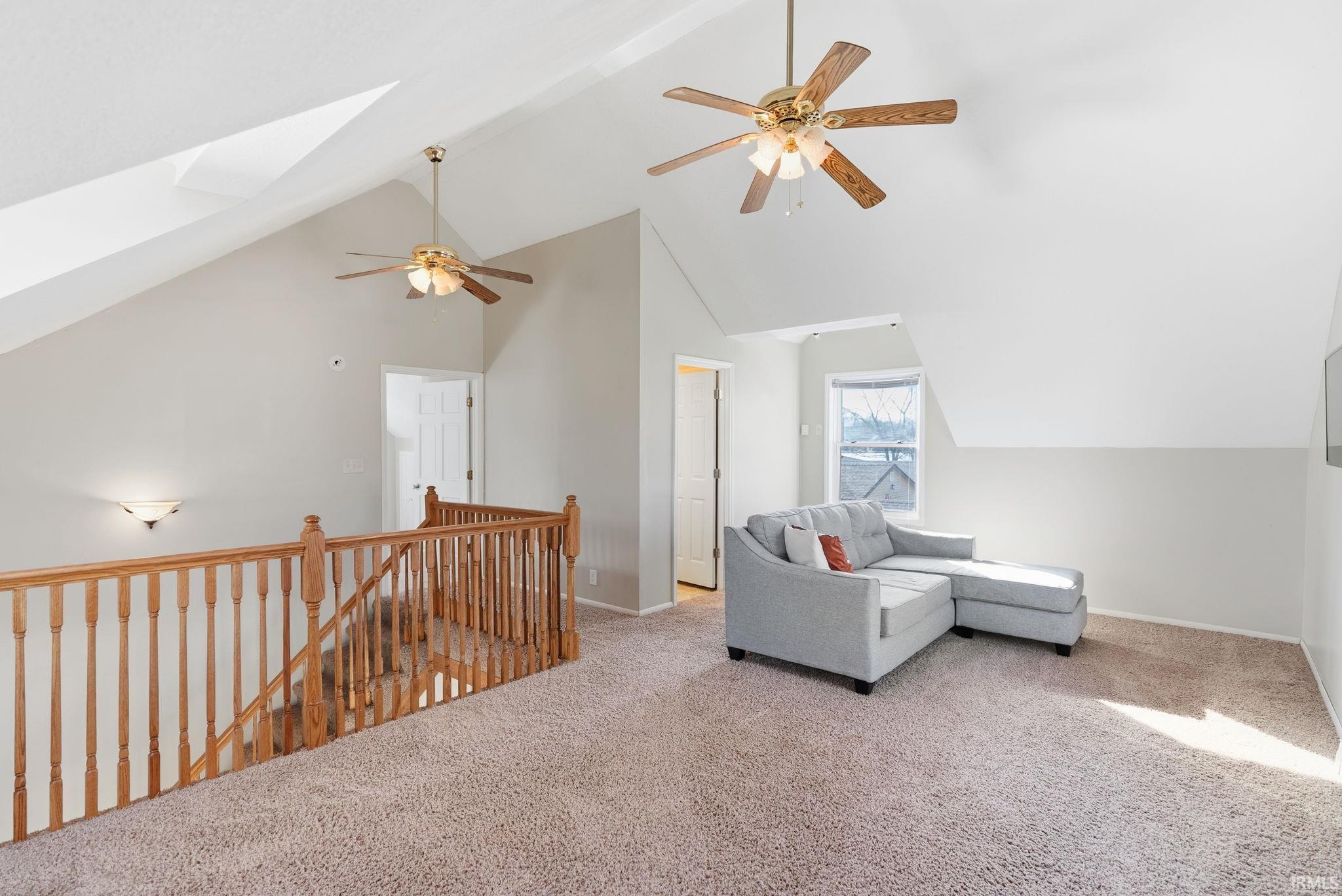 Sitting room featuring an upstairs landing, a skylight, ceiling fan, carpet floors, and a high ceiling