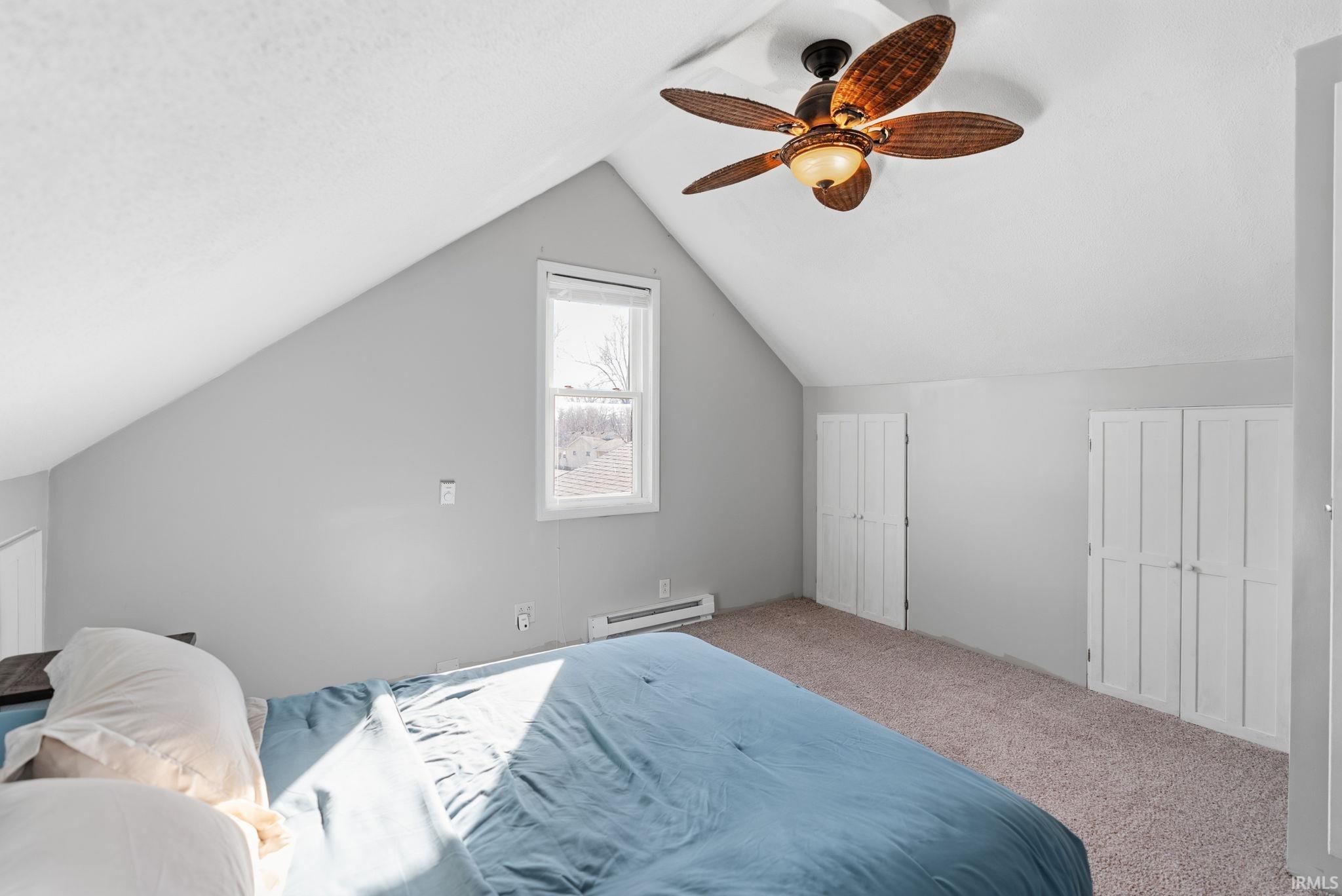 Bedroom with baseboard heating, carpet flooring, ceiling fan, and multiple closets