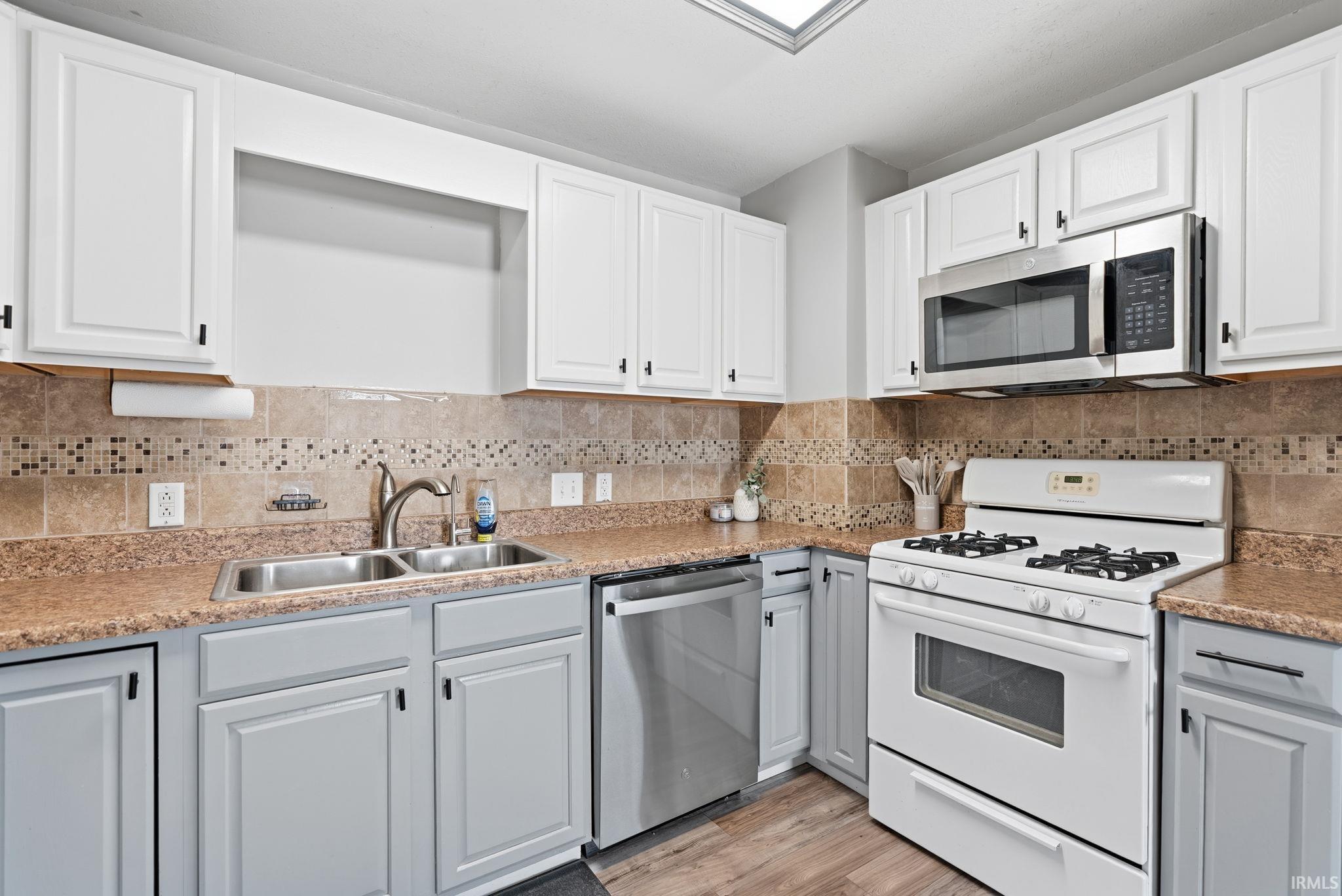 Kitchen featuring stainless steel appliances, white cabinets, light wood-type flooring, and backsplash