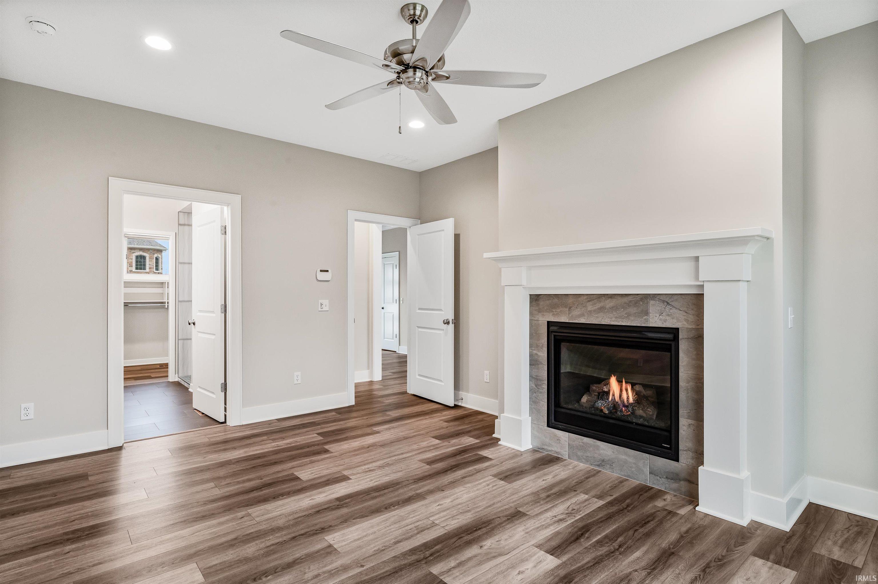 Unfurnished living room featuring a ceiling fan, a tiled fireplace, dark wood-style floors, and recessed lighting
